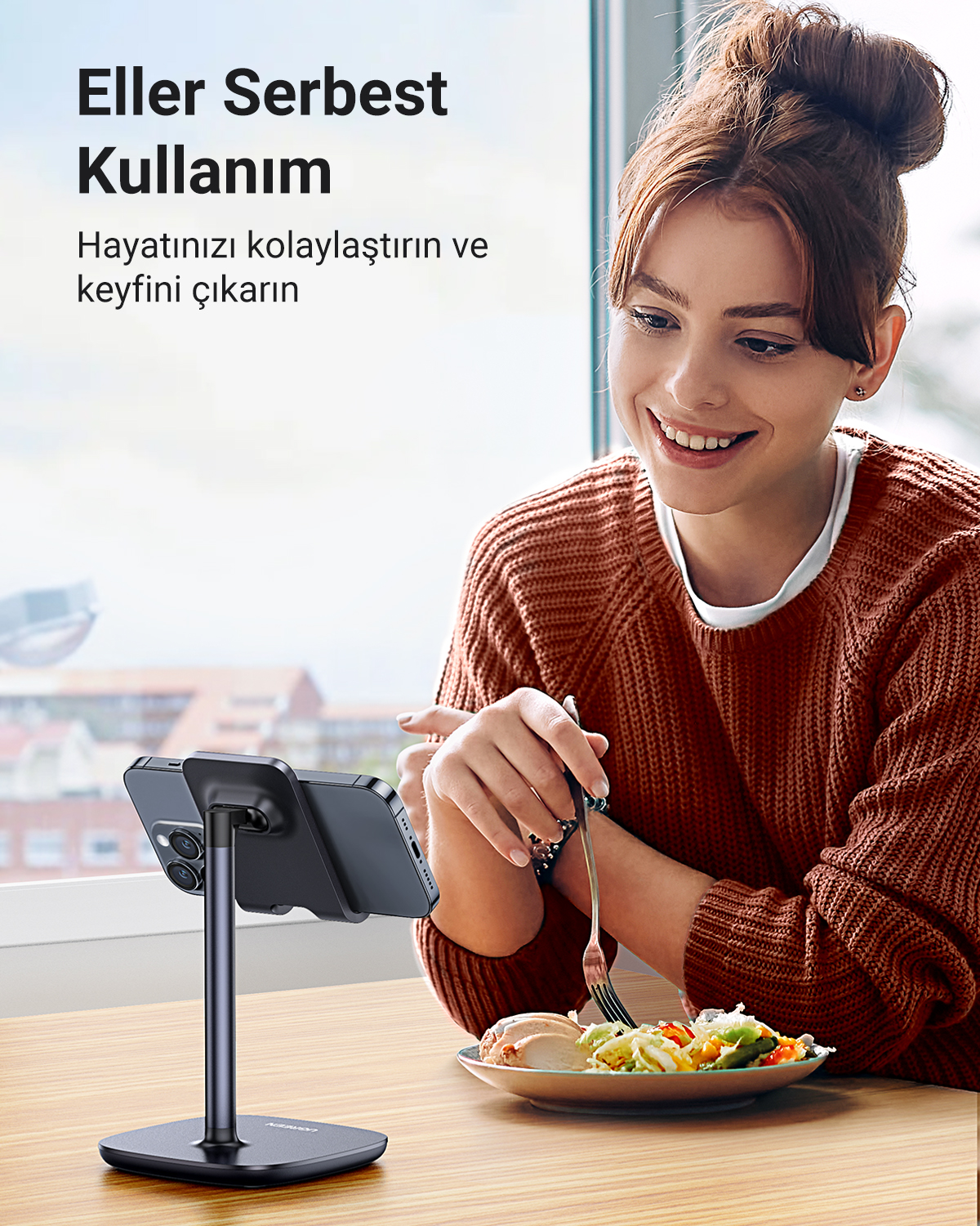 Kadın, telefonu bir stantta dururken yemek yiyor. Eller serbest kullanım.