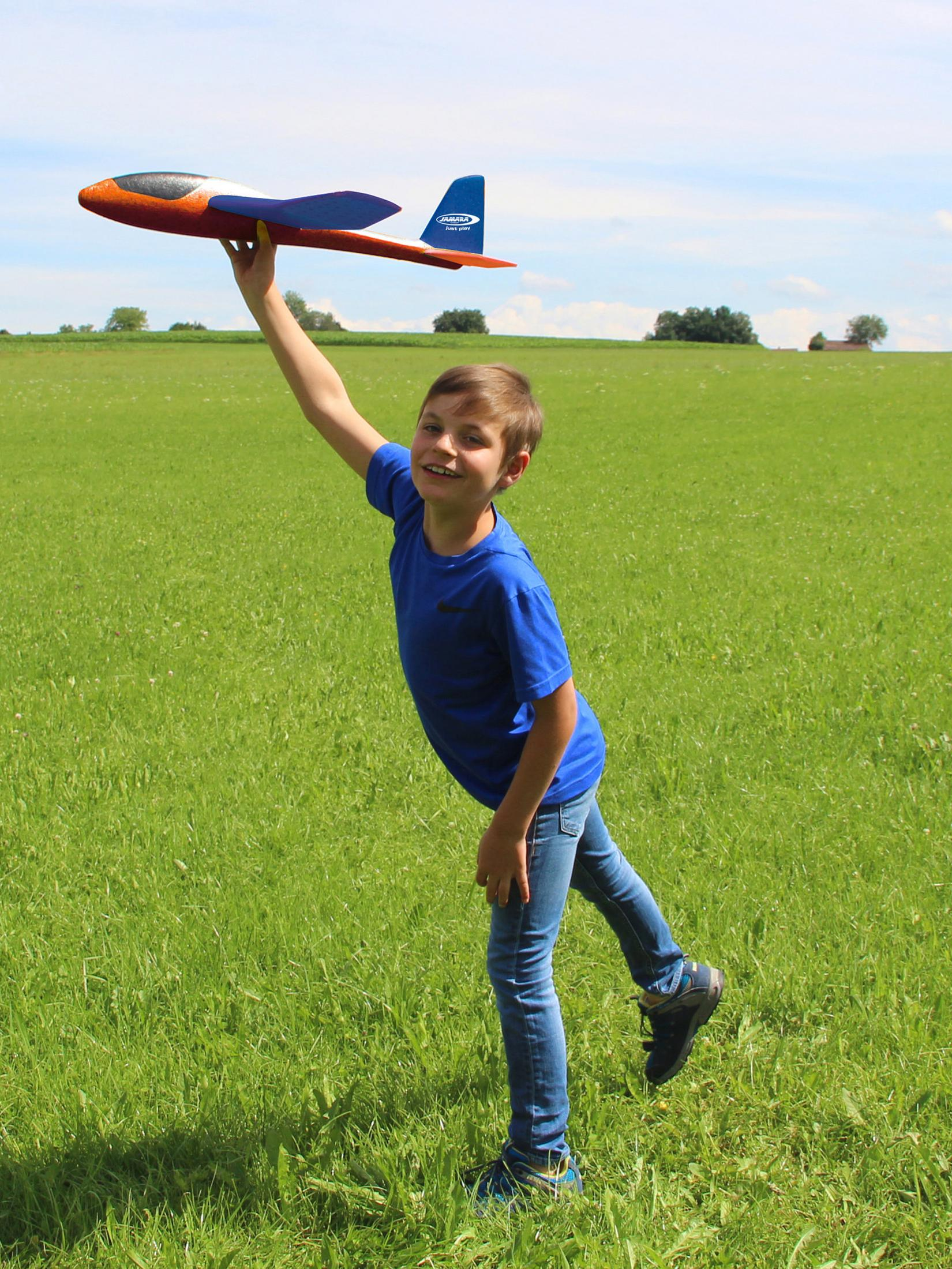 Un ragazzo tiene un aeroplano giocattolo in un campo verde.