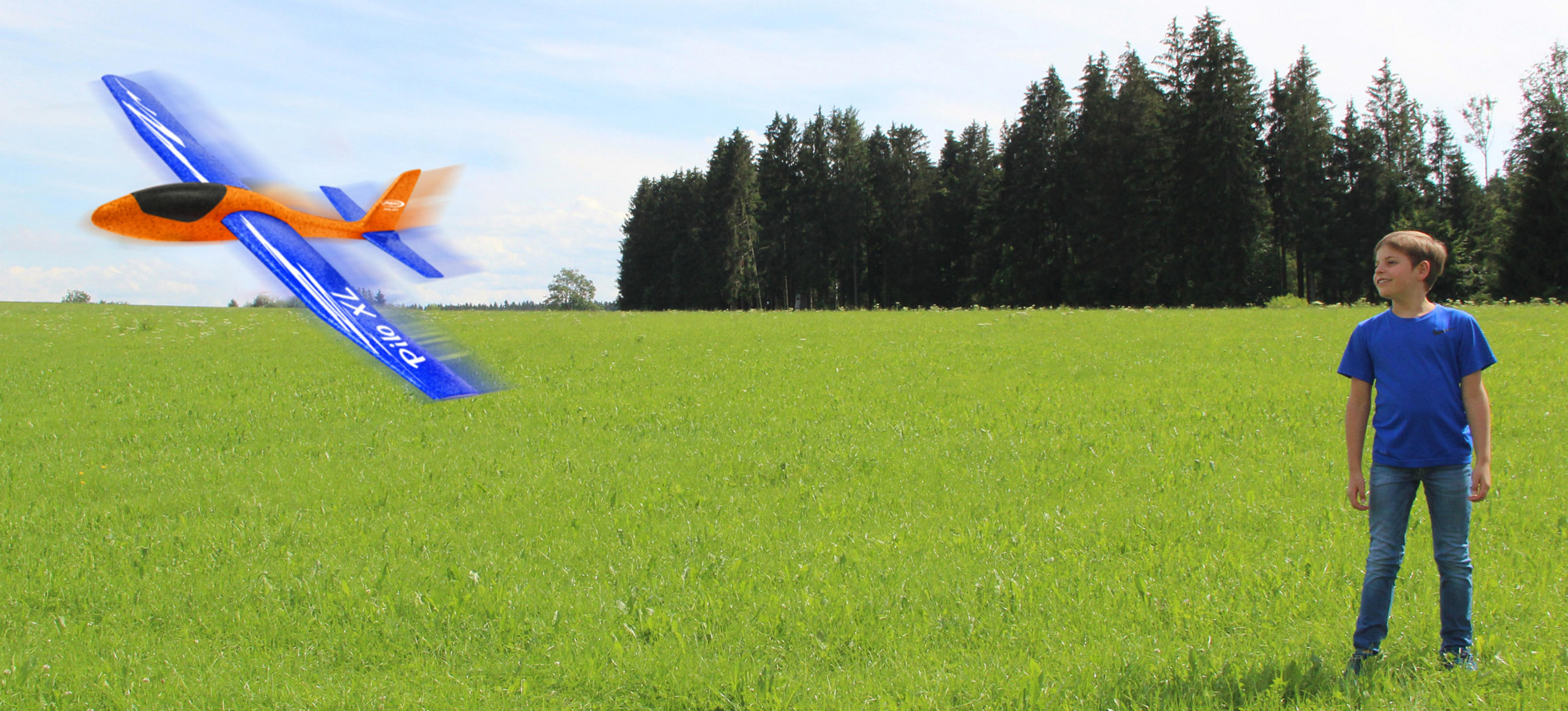 Un ragazzo è in un campo verde mentre un aereo arancione e blu vola via.