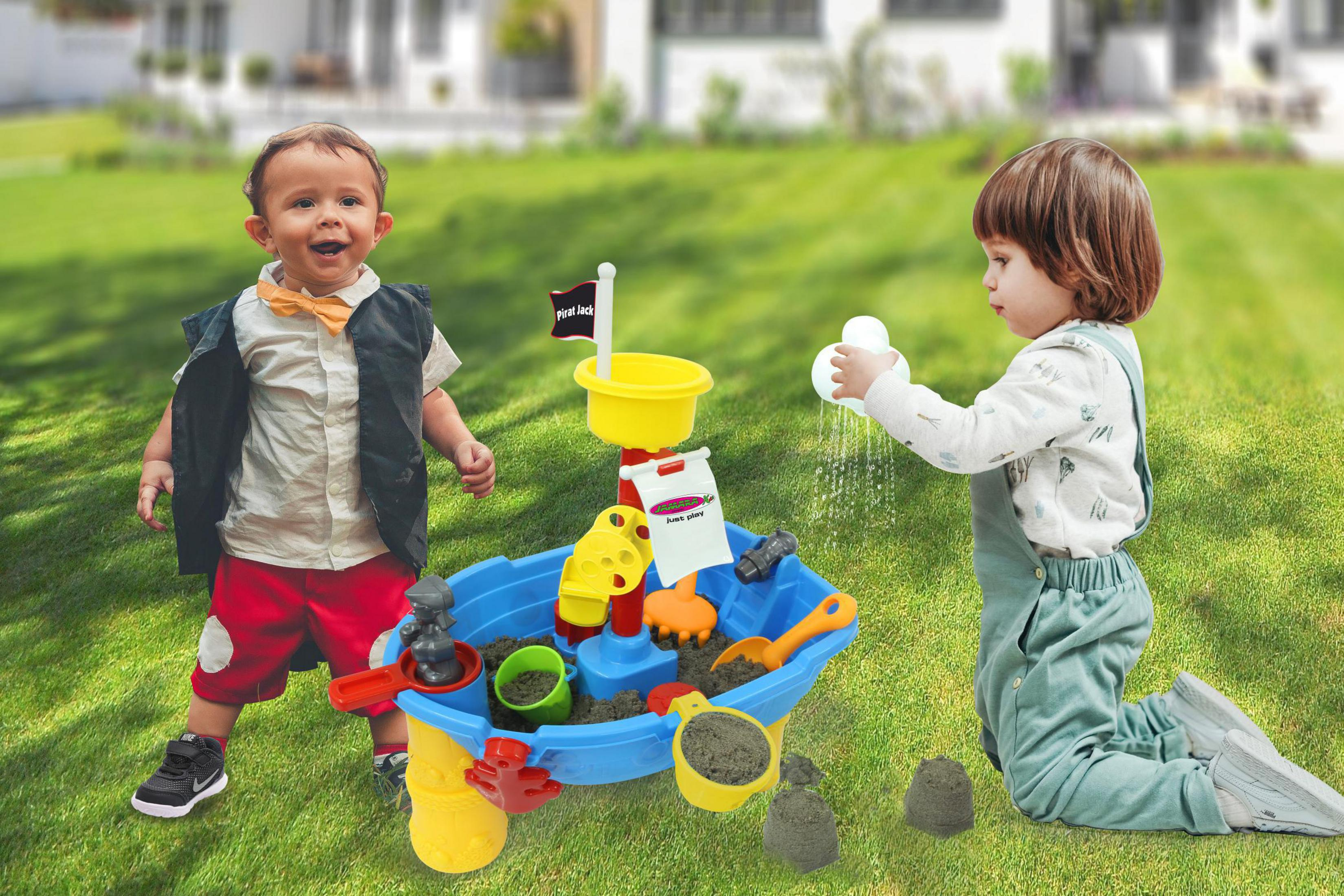 Dos niños juegan en un arenero al aire libre. Uno sonríe, el otro vierte agua.