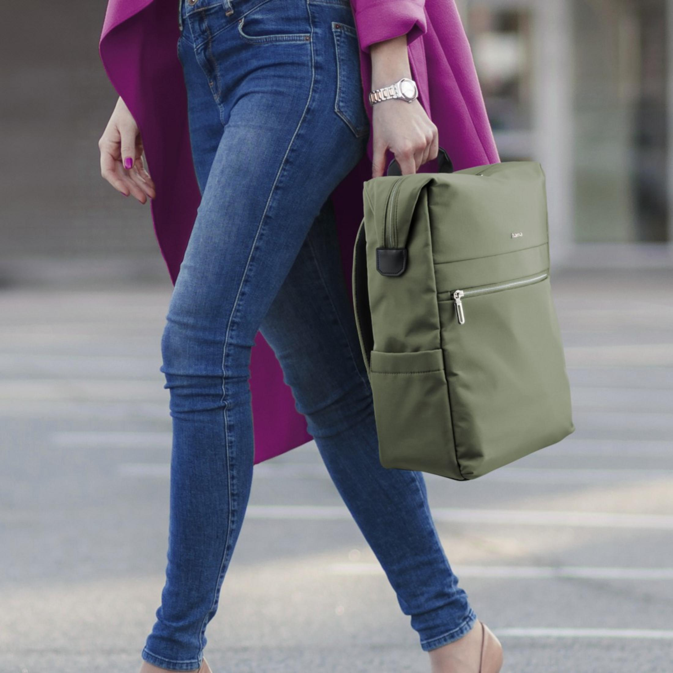 Una donna in jeans e cappotto viola porta uno zaino verde.
