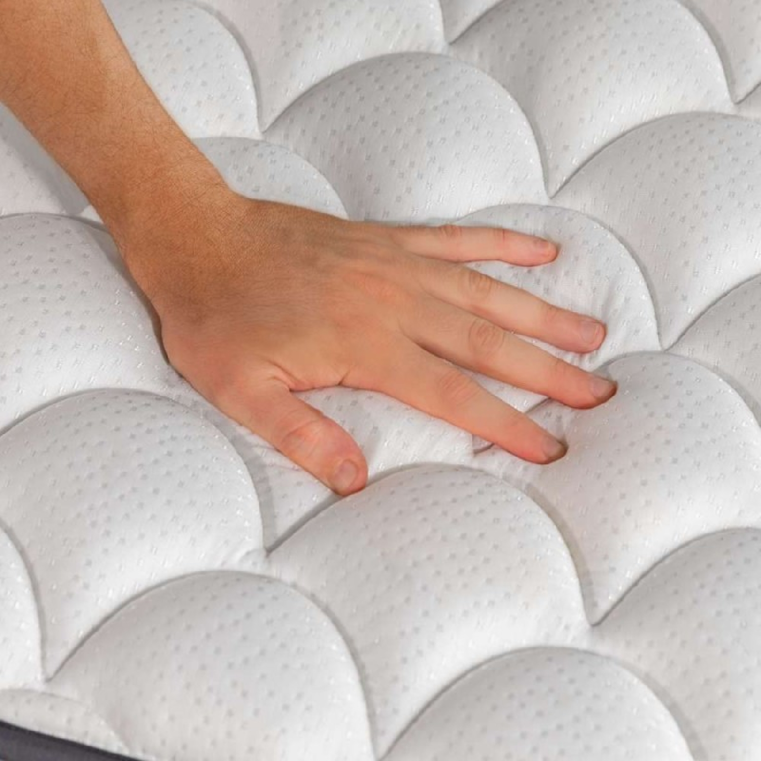 Una mano presiona un colchón blanco acolchado con un patrón ondulado.