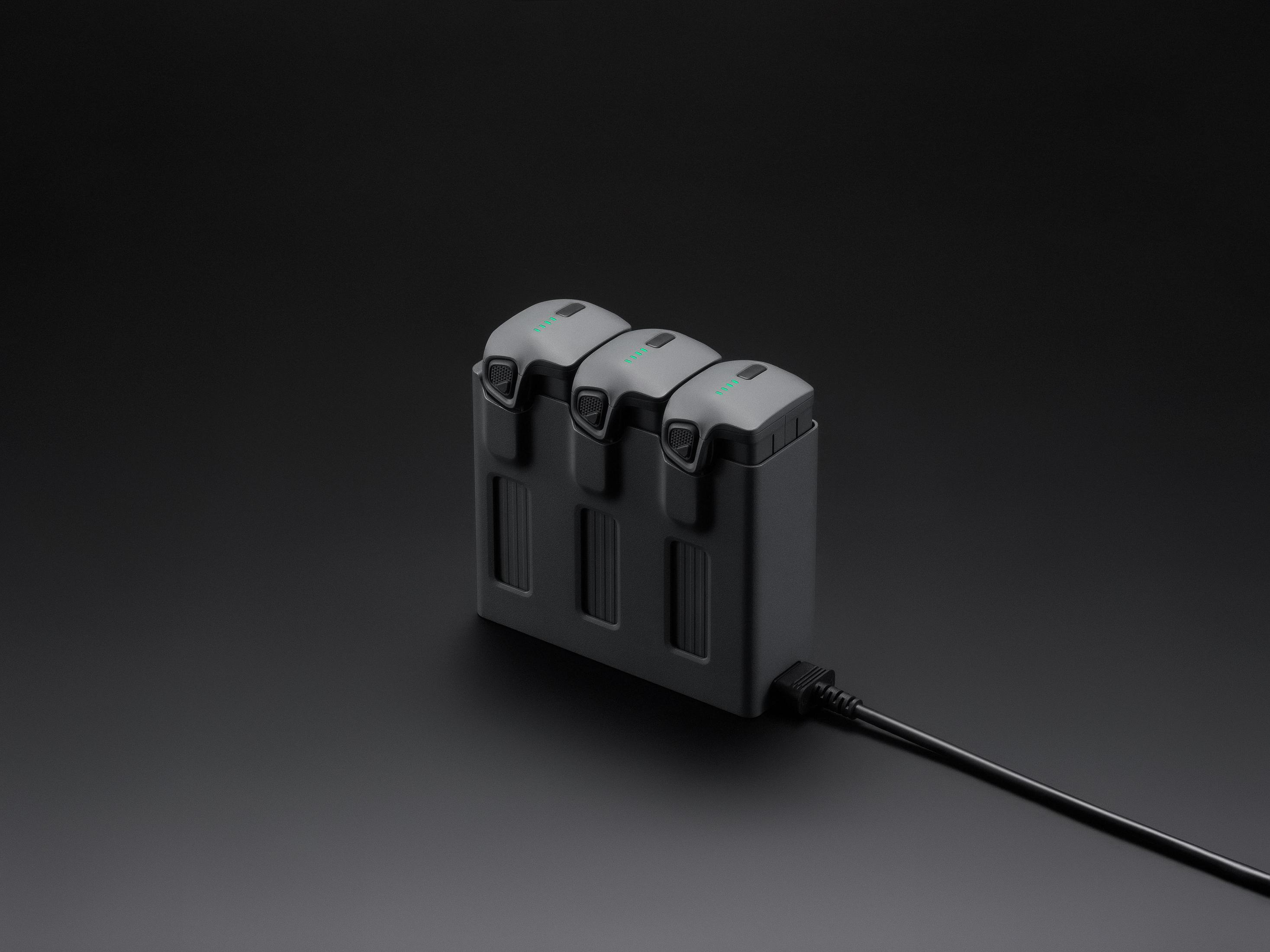 Tre batterie grigie in un'unità di ricarica su sfondo nero.