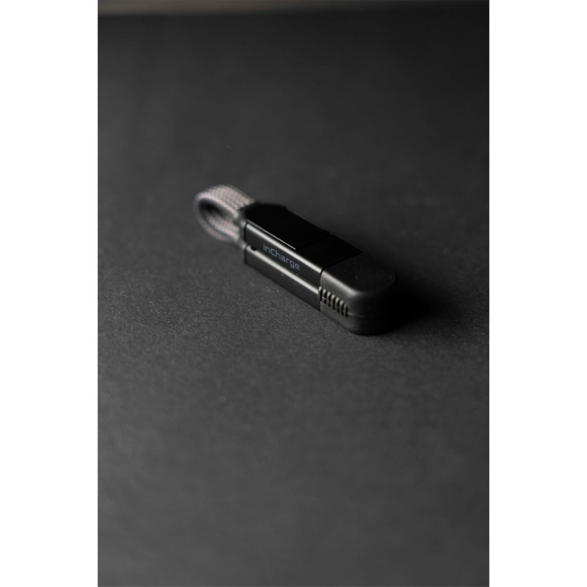 Ein schwarzer USB-Stick mit einer grauen Schlaufe liegt auf einer dunklen, texturierten Oberfläche.
