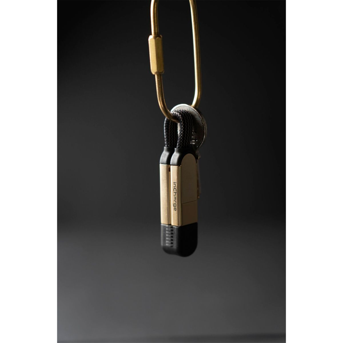 Ein goldener Karabinerhaken hält zwei schwarze Ladekabel mit goldenen Enden.