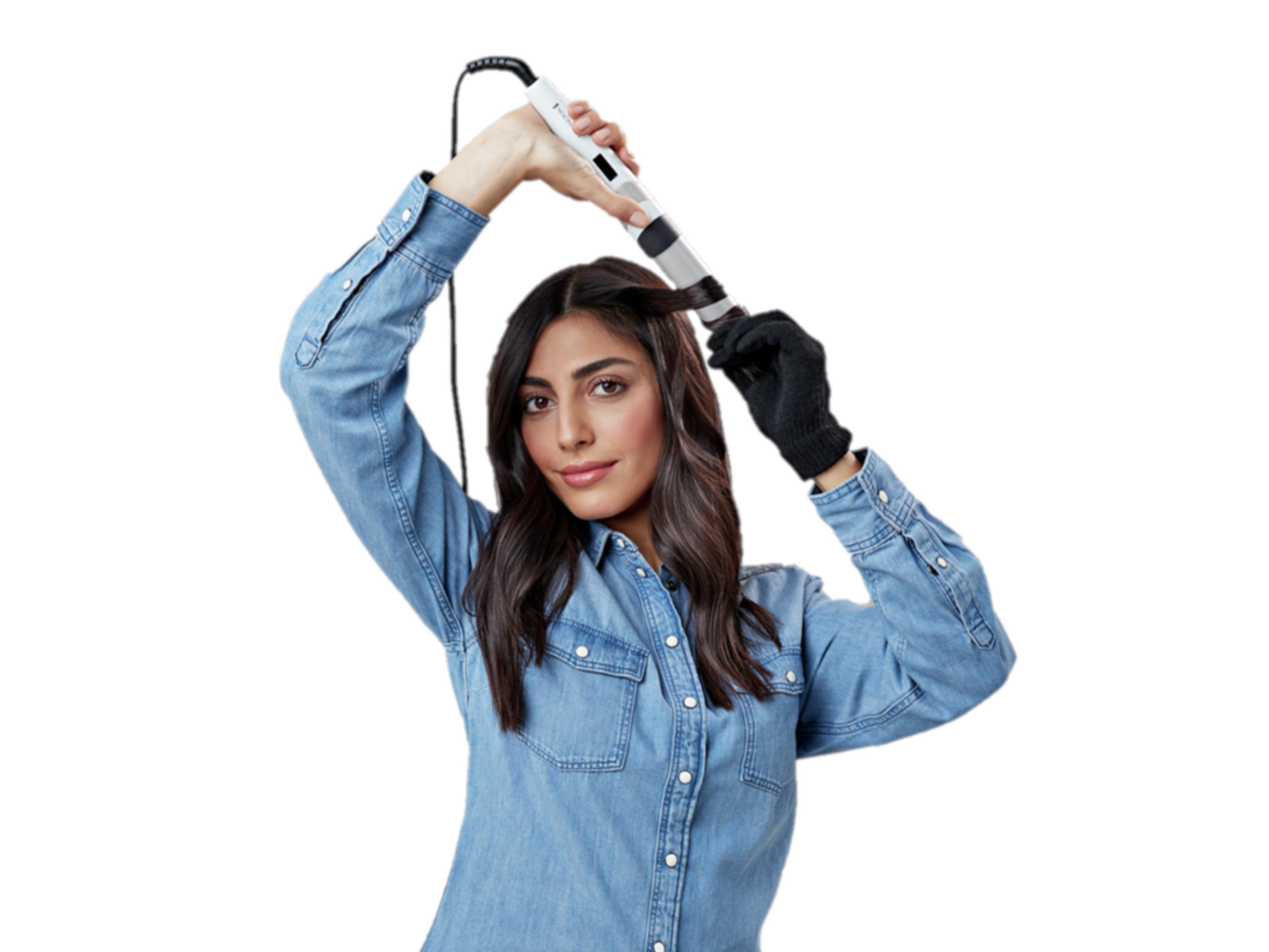 Una donna con i capelli scuri si arriccia i capelli con un arricciacapelli bianco.