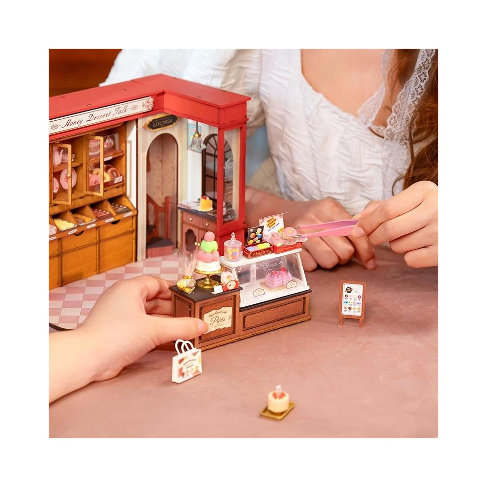Panetteria in miniatura con espositore, porta torta e mani con pinzette.