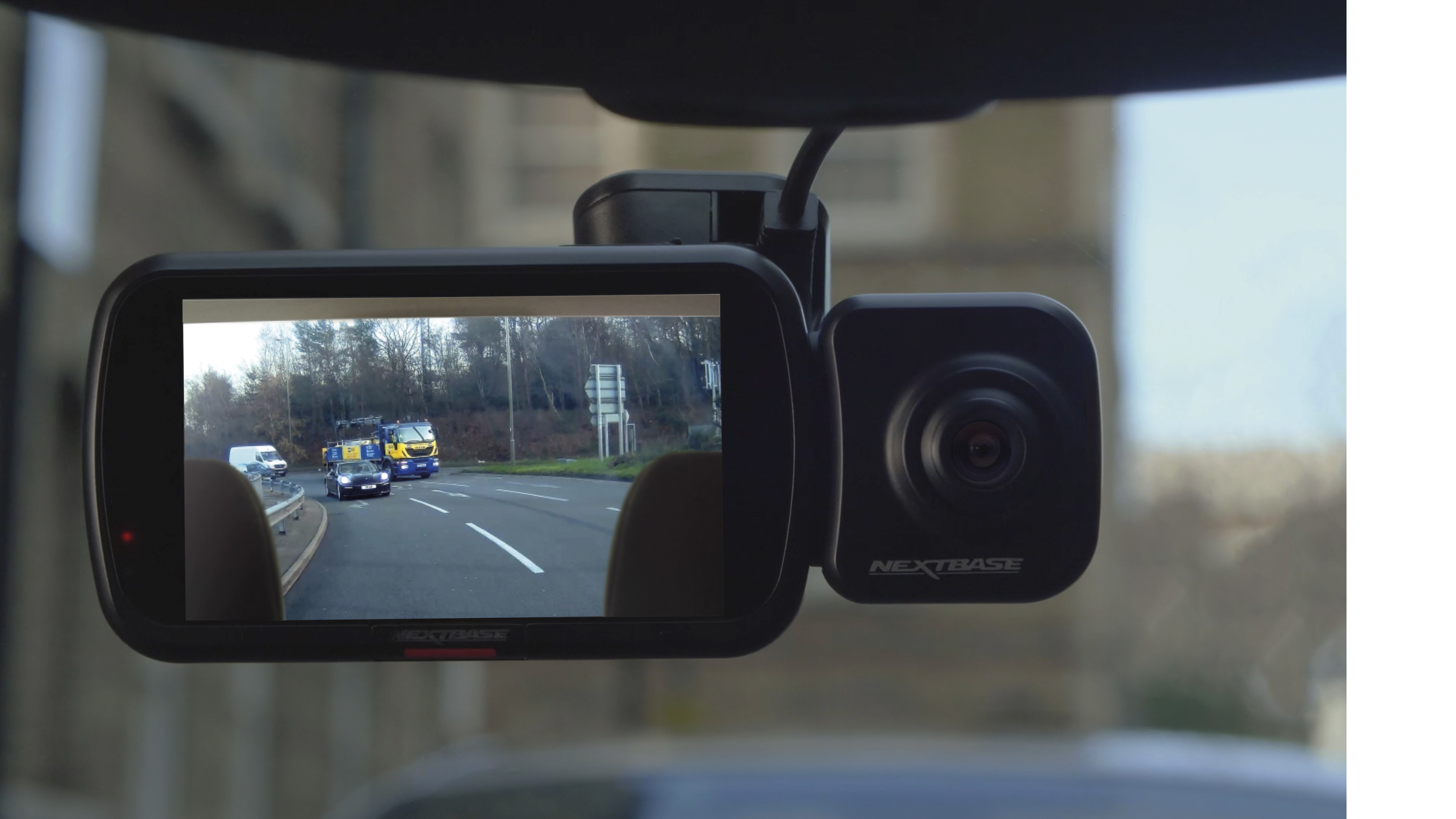 Dashcam-Ansicht: Ein schwarzes Auto und ein gelber LKW auf einer Straße. Bäume im Hintergrund.