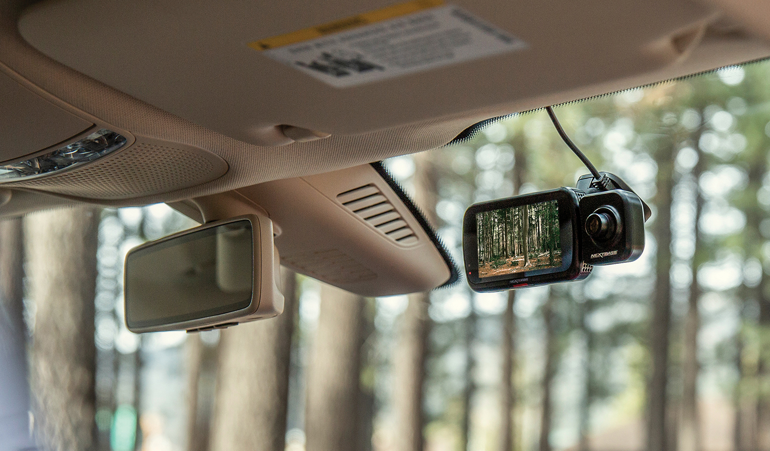 Auto-Innenraum mit Dashcam, die einen Wald zeigt, und Rückspiegel.