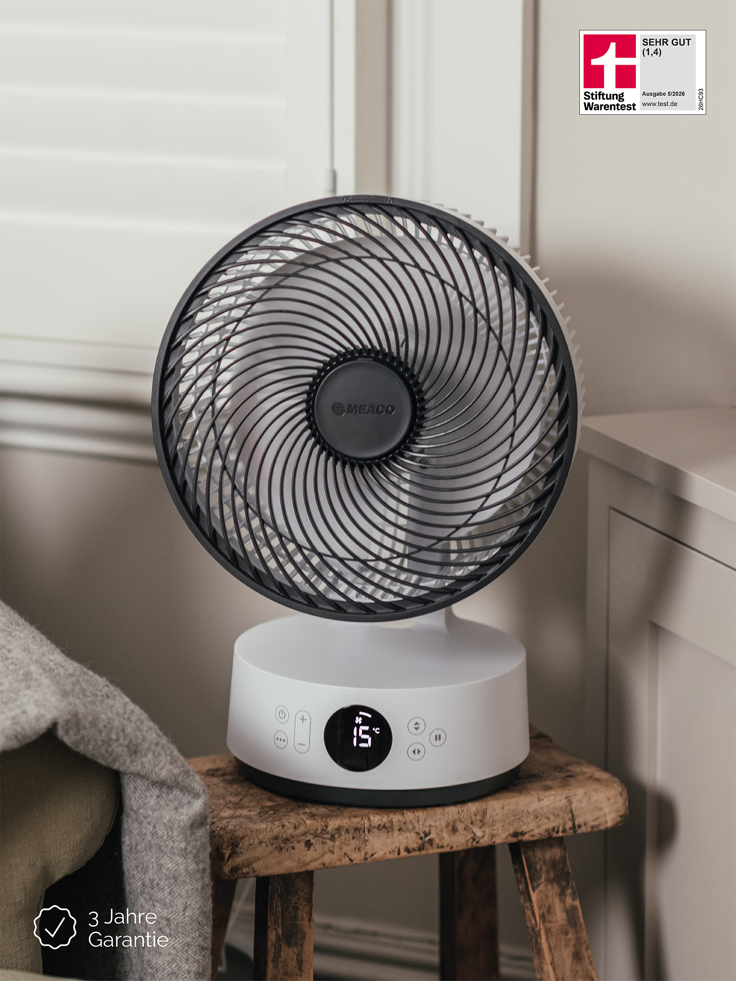 Un ventilatore bianco con griglia nera è seduto su uno sgabello di legno. Un sigillo mostra 