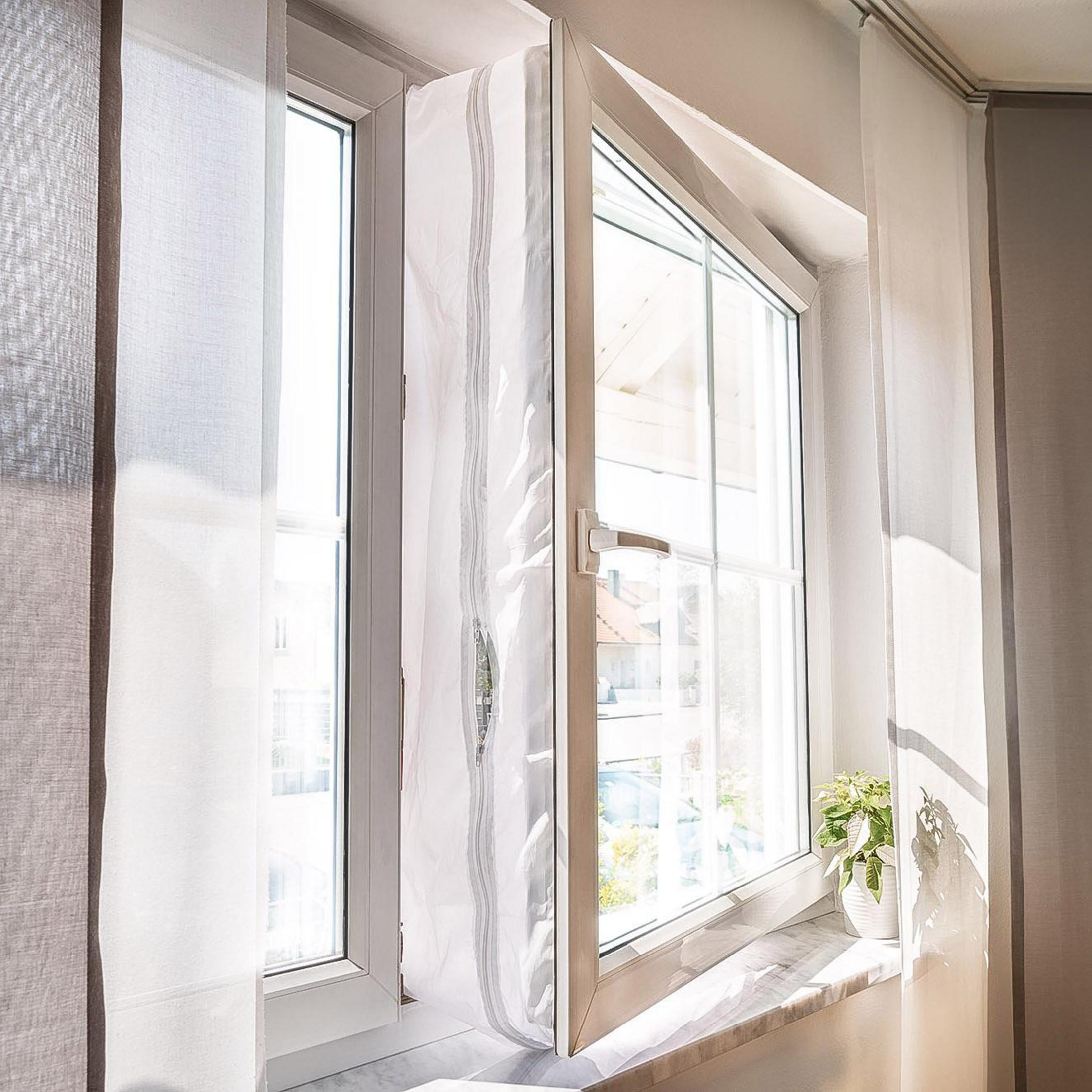 Ein offenes Fenster mit weißen Vorhängen und einer Topfpflanze auf dem Sims.
