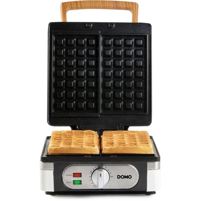 Una piastra per waffle aperta con due waffle cotti e manico in legno.