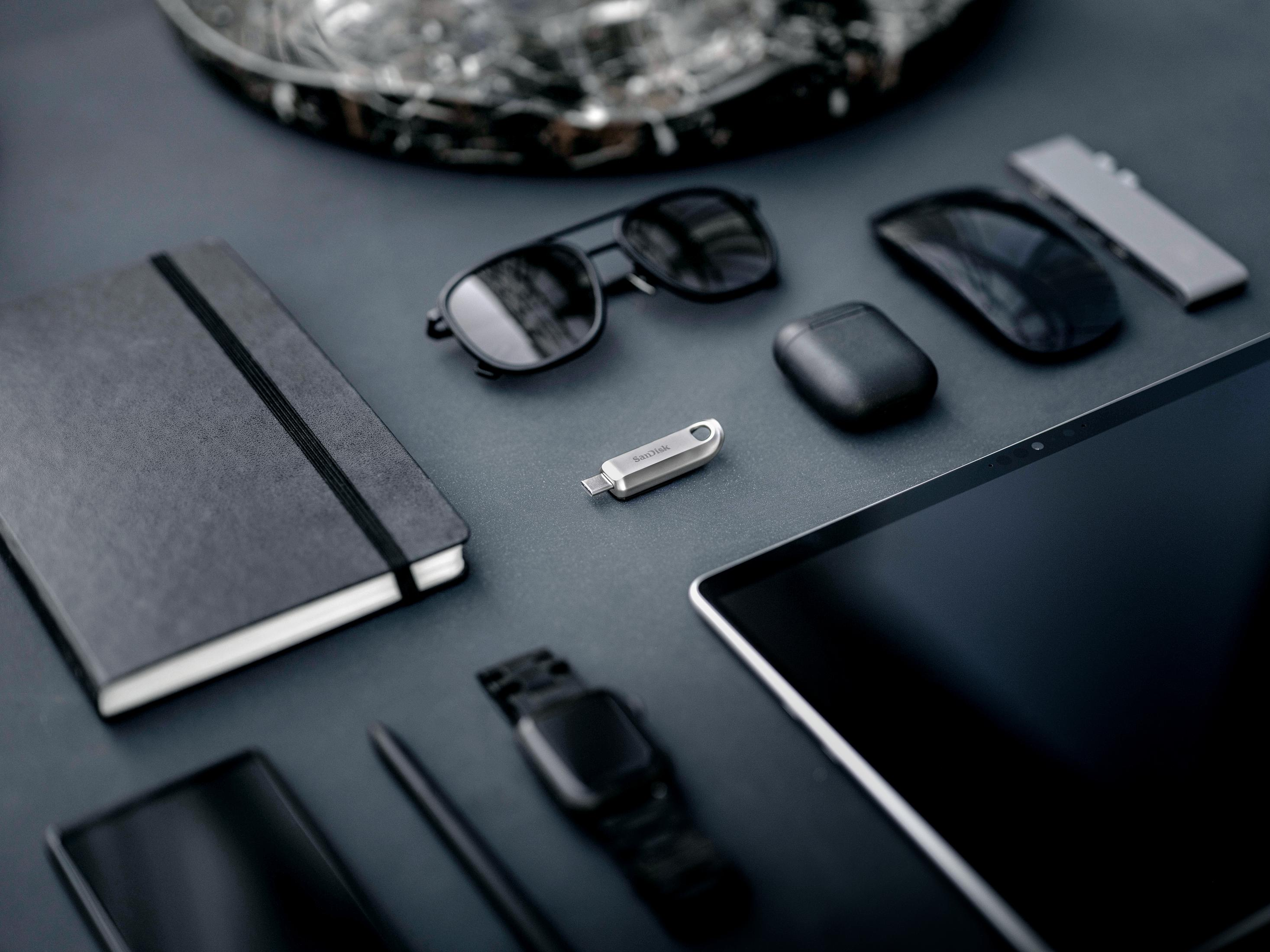 Taccuino nero, occhiali da sole, mouse, penna, orologio, unità USB, AirPods e tablet.