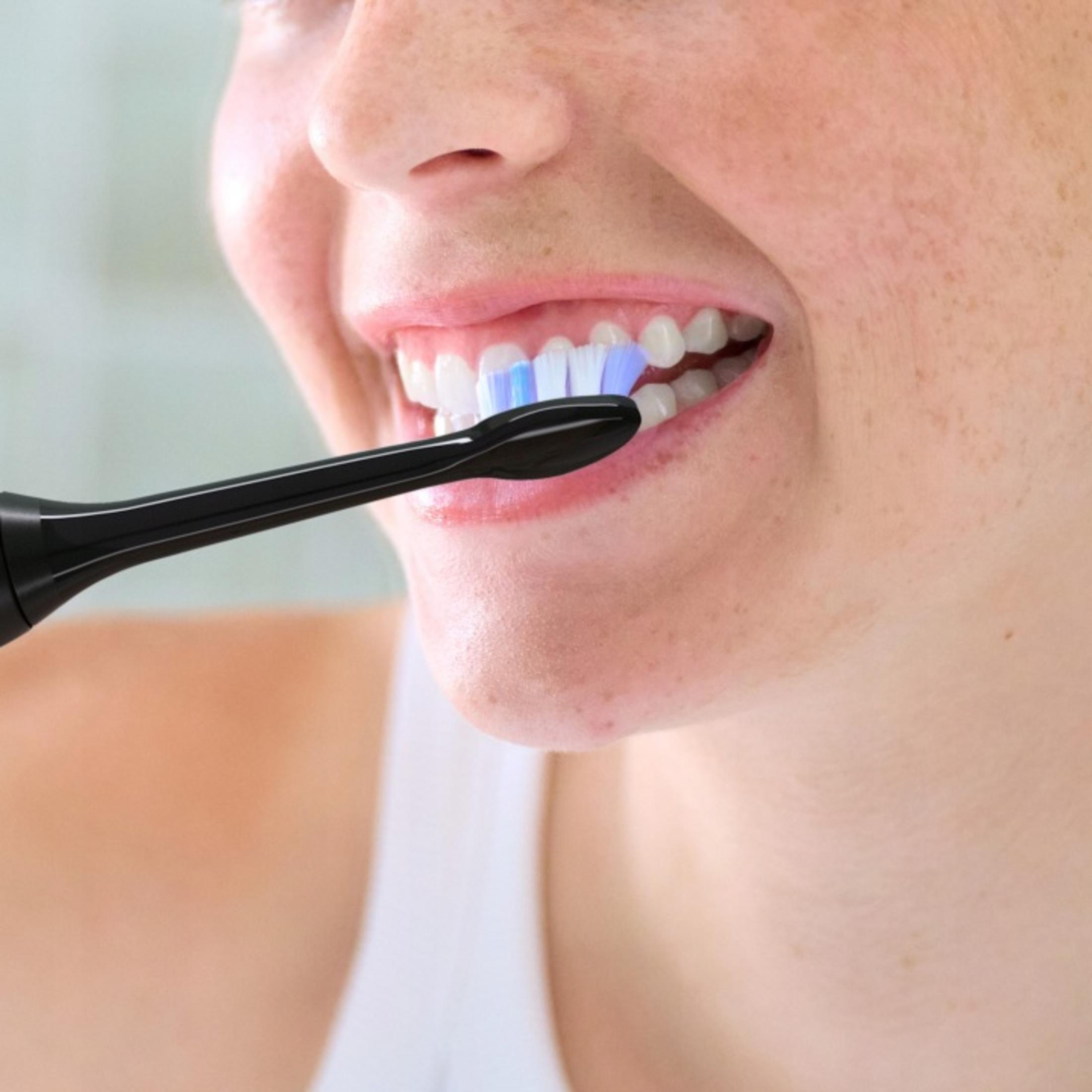 Una persona si lava i denti con uno spazzolino elettrico.