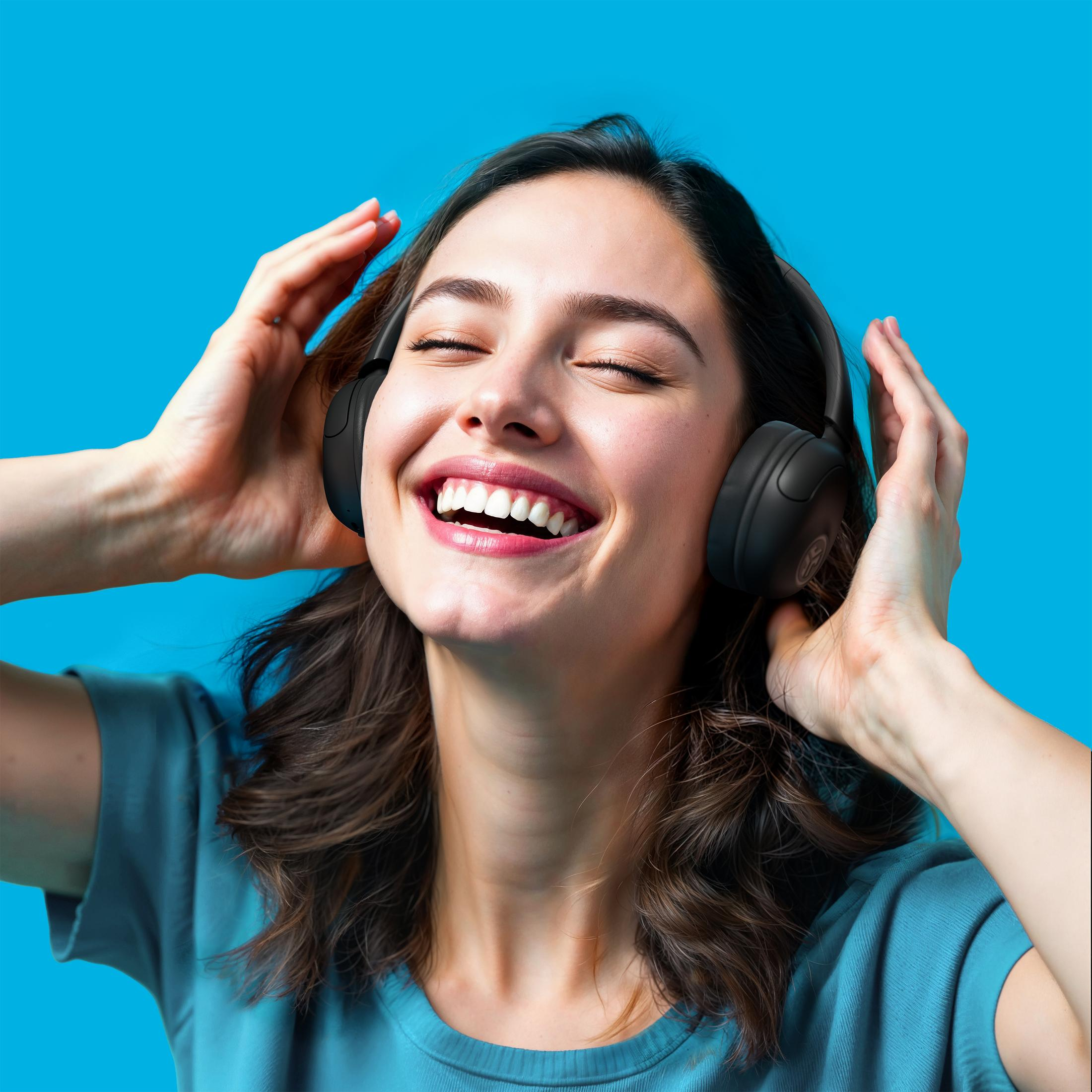 Une femme souriante, les yeux fermés, écoute de la musique avec un casque.