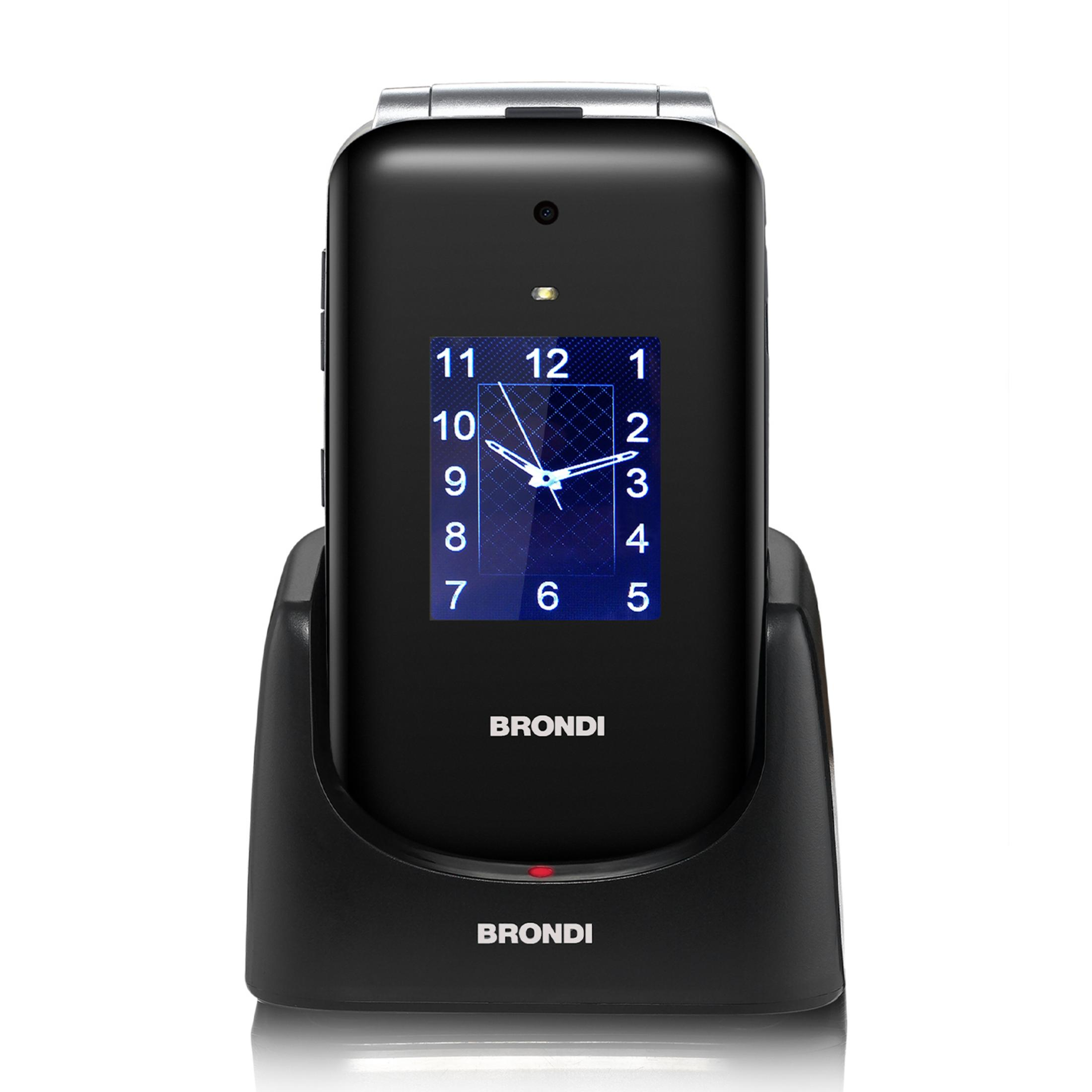 Teléfono plegable negro con reloj en base de carga. Logo Brondi visible.
