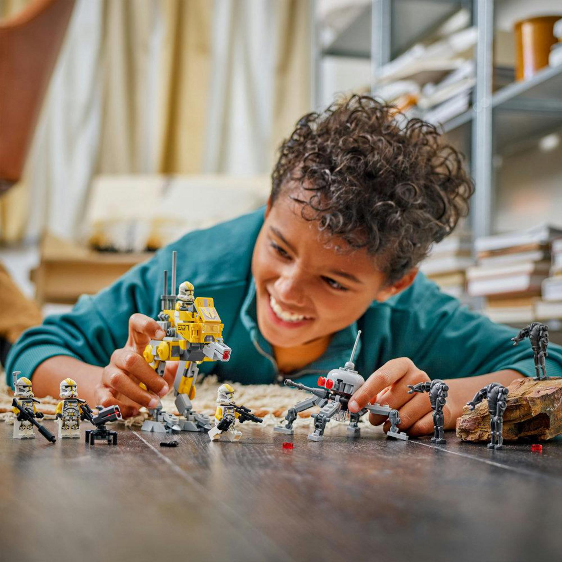 Un ragazzo gioca con personaggi Lego di Star Wars, tra cui un camminatore giallo e droidi.
