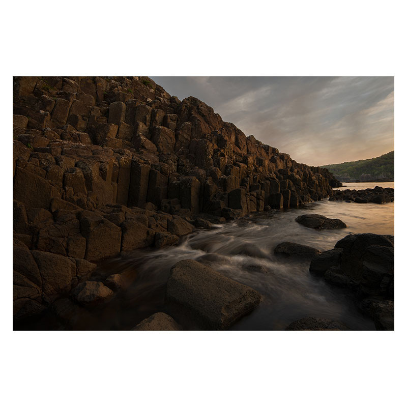 Formations rocheuses en colonnes au bord de la mer au coucher du soleil avec mouvement d'eau.