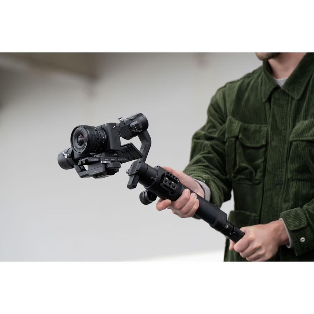 Een persoon in een groen corduroy jasje houdt een gimbal met camera vast.