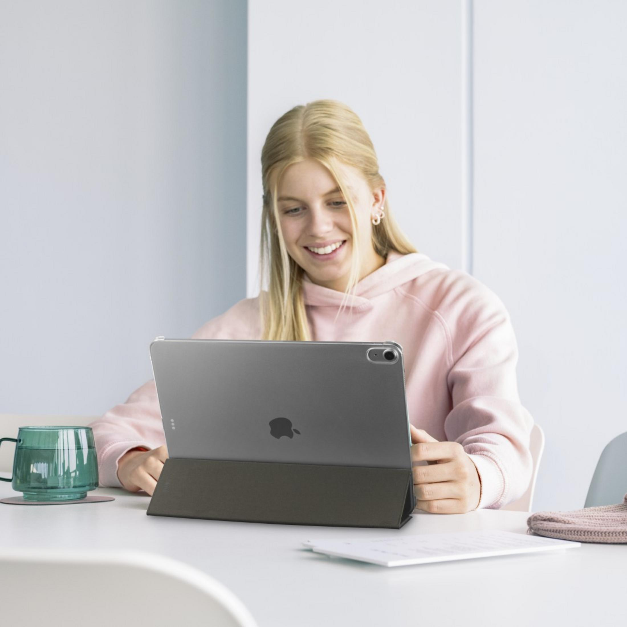 Ein junges blondes Mädchen in einem rosa Hoodie benutzt ein Tablet. Daneben ein grüner Becher.