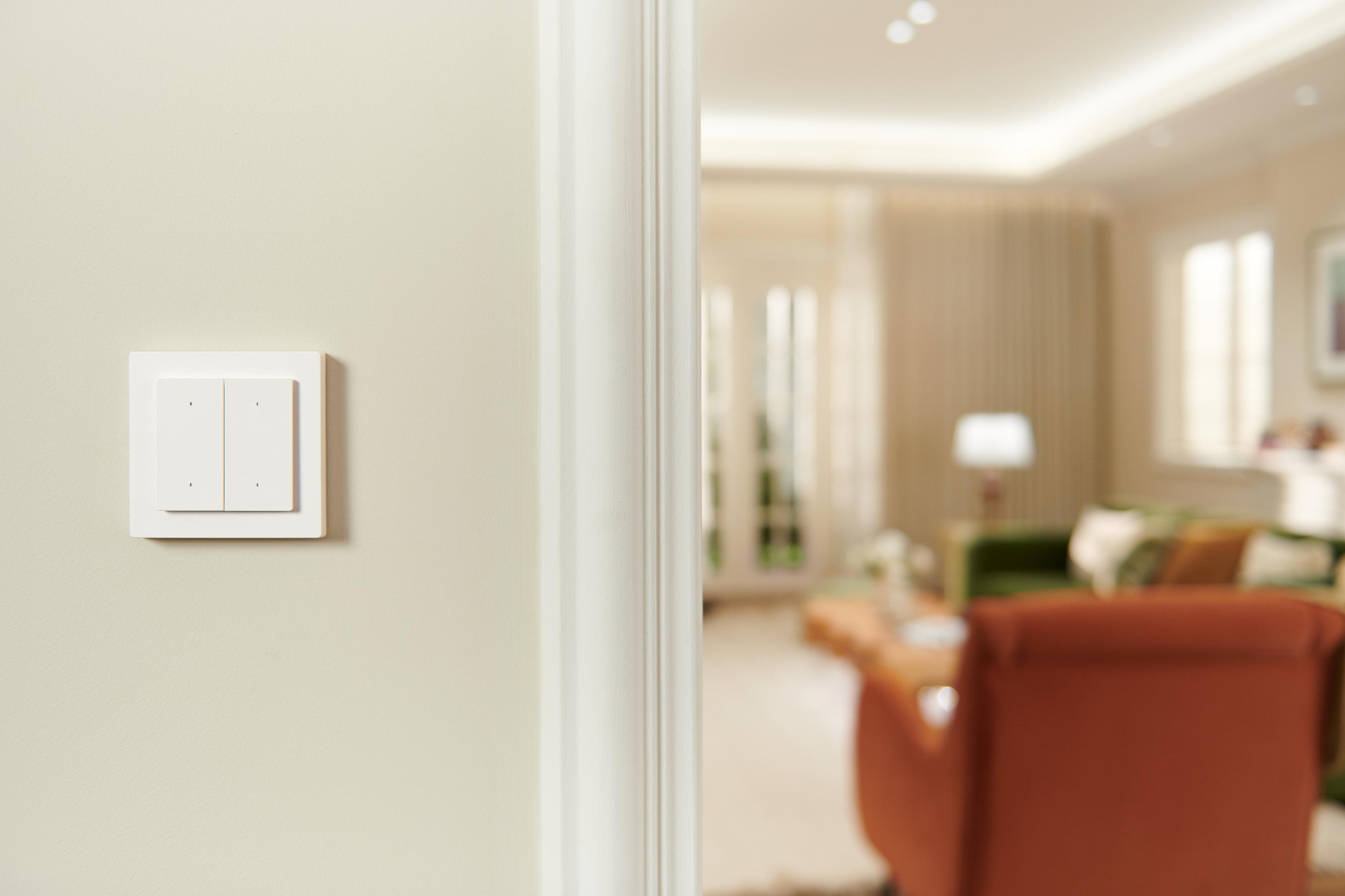 Un interrupteur blanc à quatre boutons sur un mur beige clair.