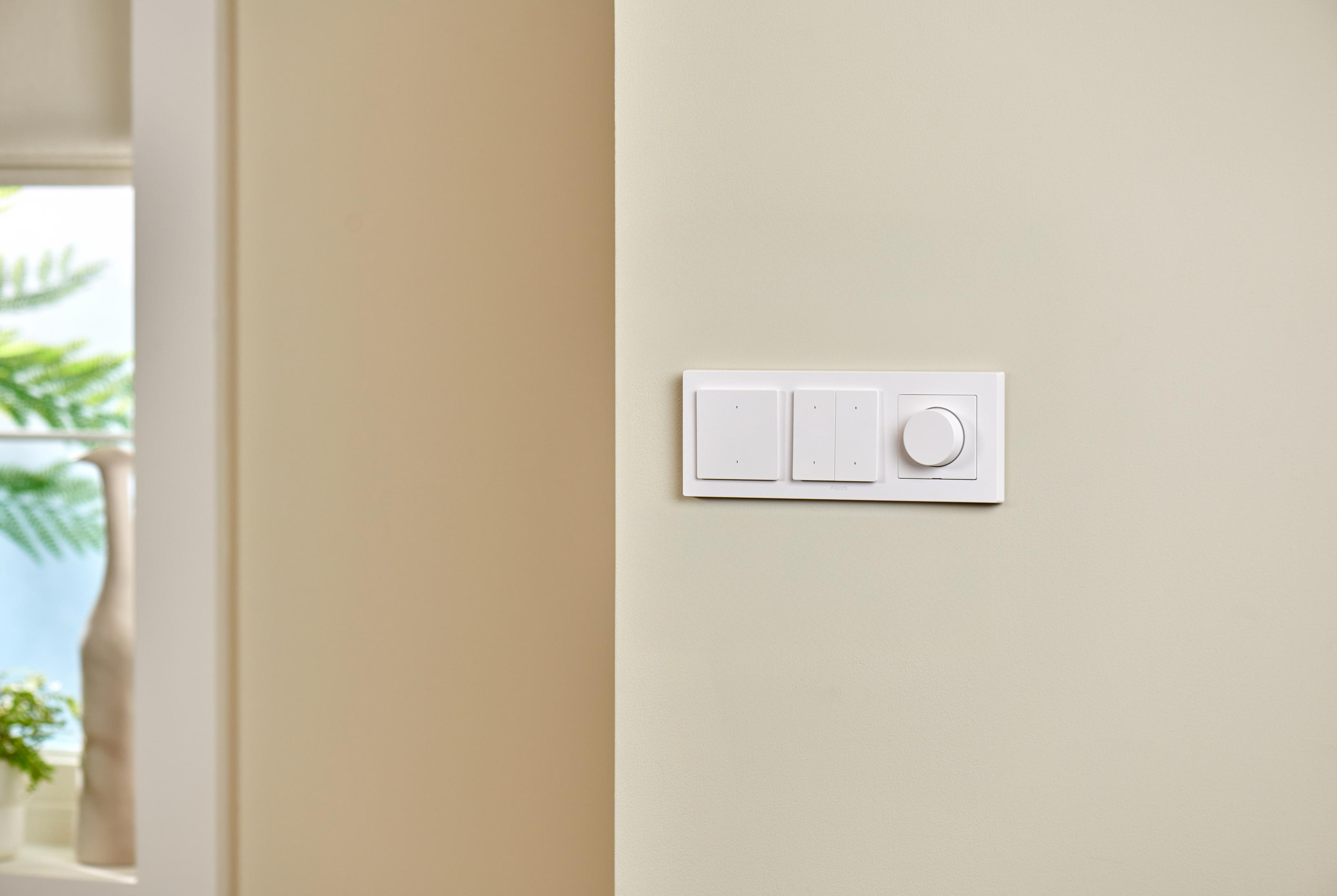 Un interrupteur blanc avec trois boutons et une molette sur un mur crème.