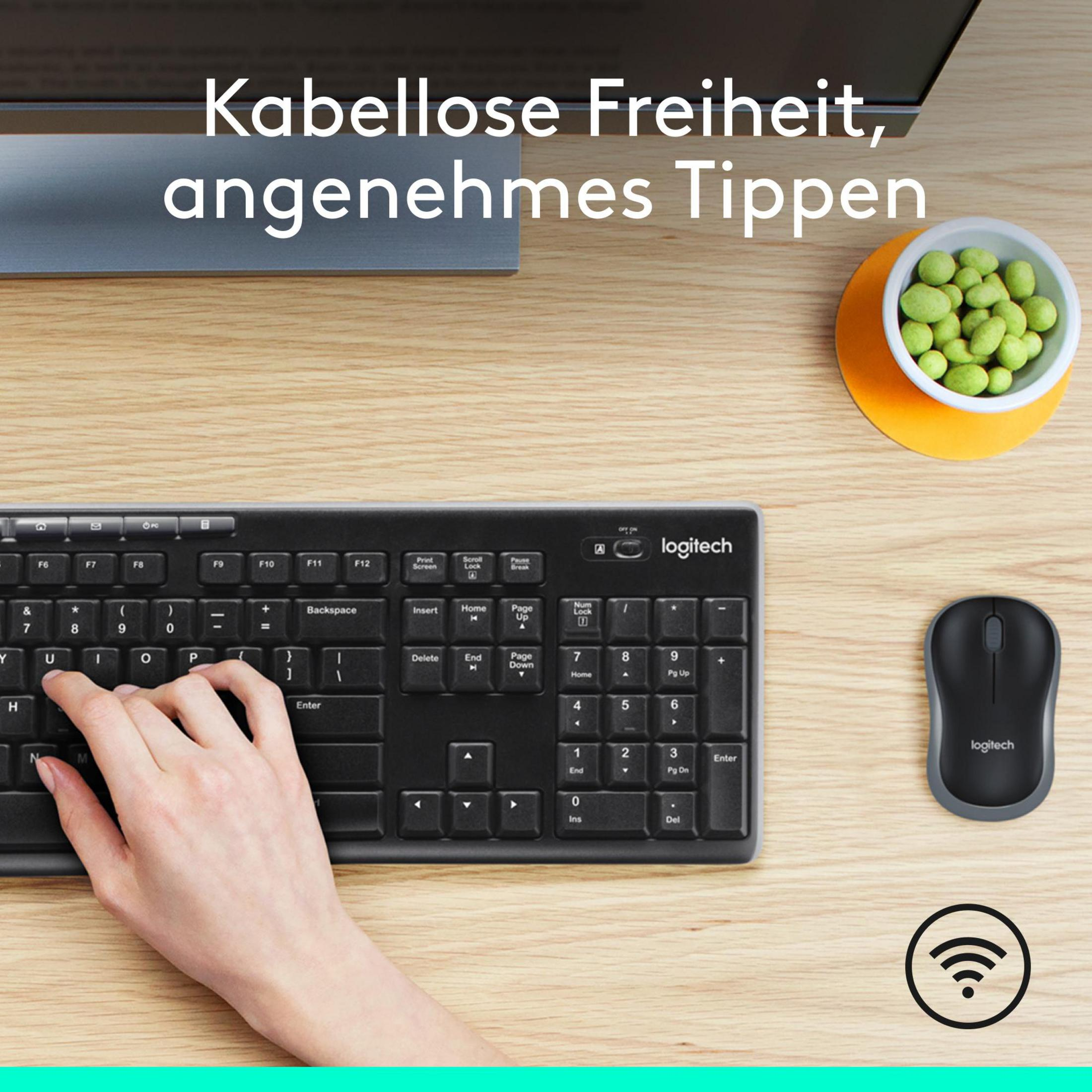Tastiera e mouse Logitech neri su legno, con ciotola di arachidi.