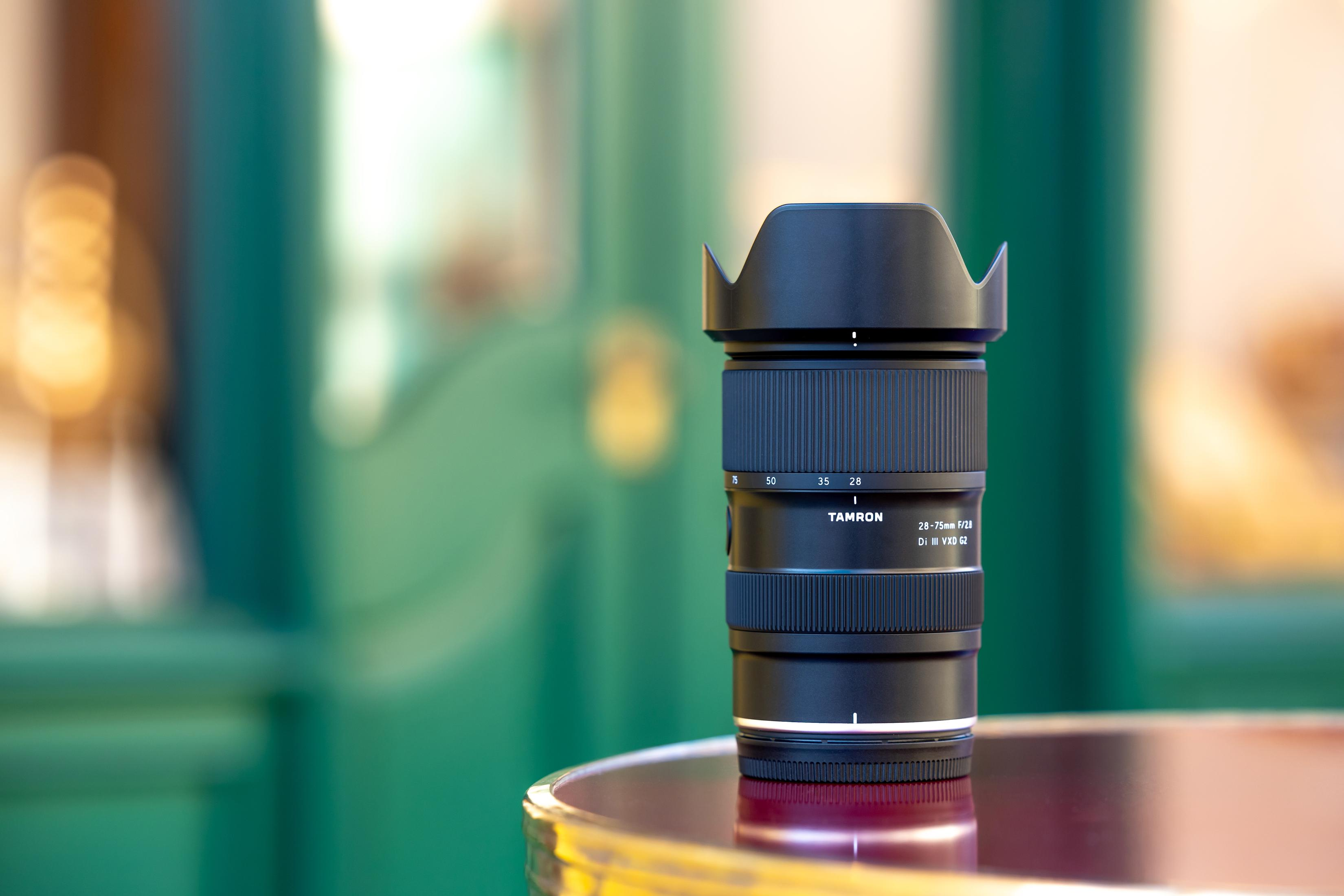 Ein schwarzes Tamron 28-75mm f/2.8 Objektiv mit Gegenlichtblende auf einem Tisch.