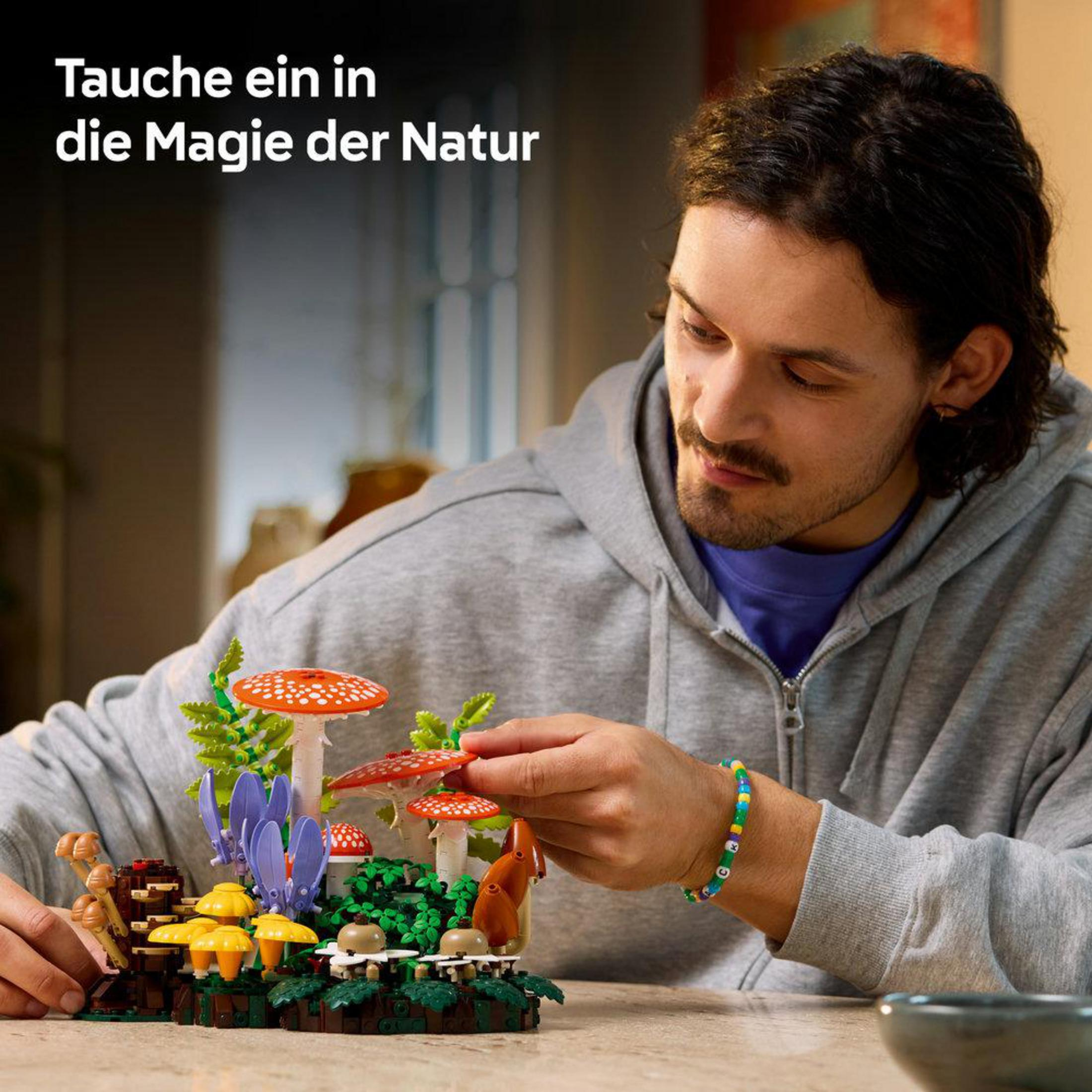 Un uomo costruisce un set di funghi Lego con funghi rossi e gialli e piante verdi.