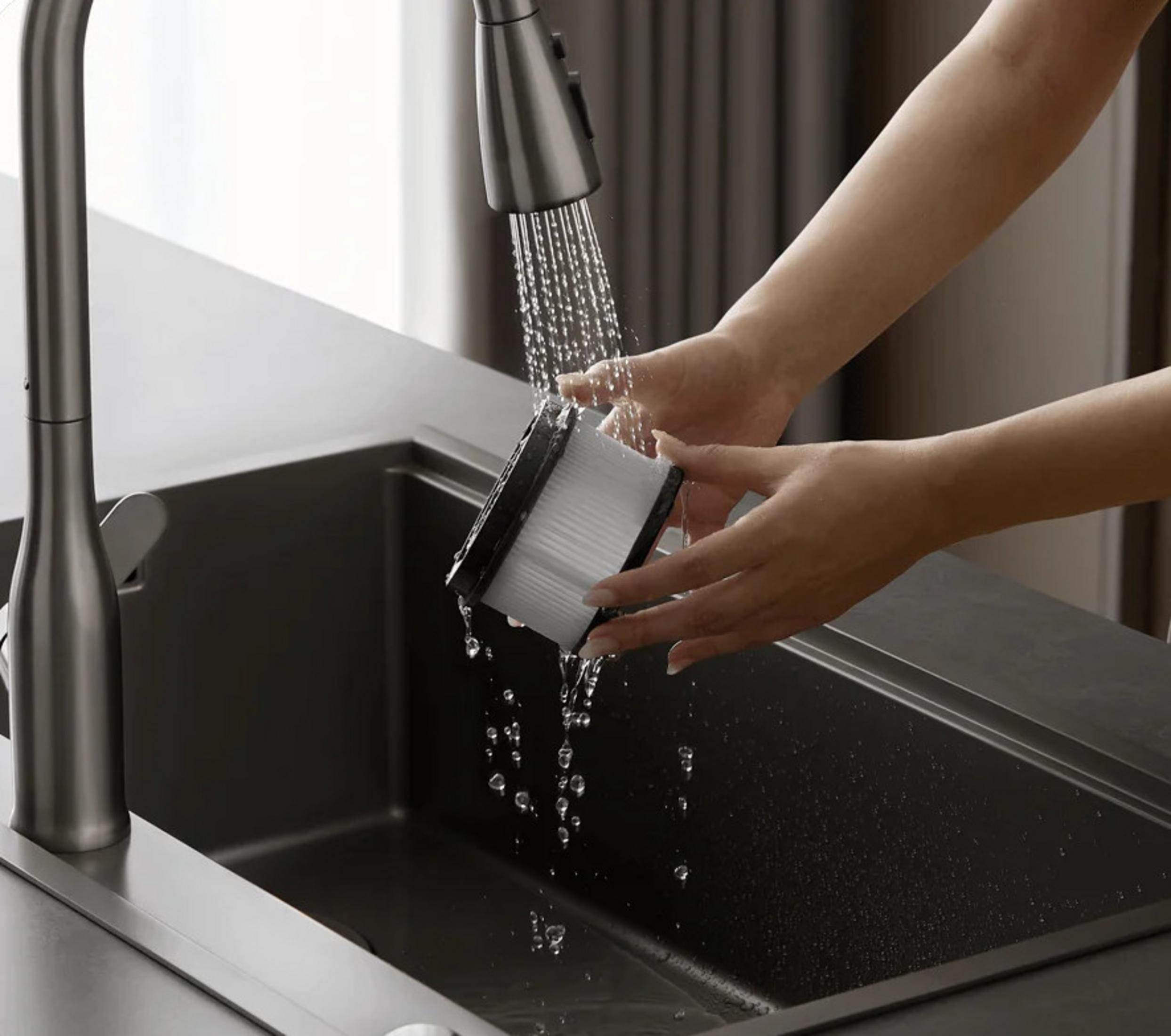 Una mano sciacqua una spazzola sotto l'acqua corrente in un lavello.