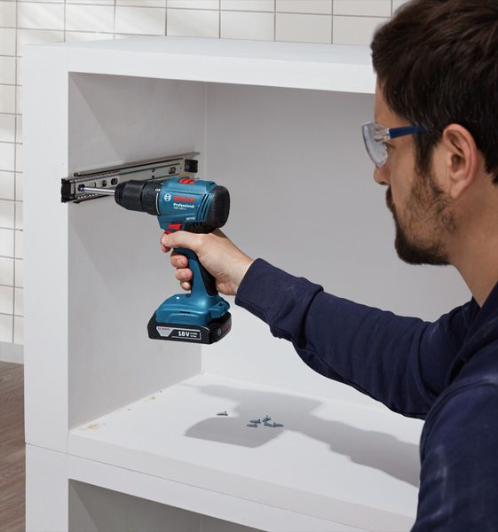 Uomo con occhiali protettivi fora mobile bianco con trapano a batteria.