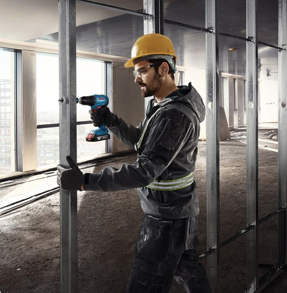 Un uomo con elmetto fora montanti metallici per un muro in cantiere.