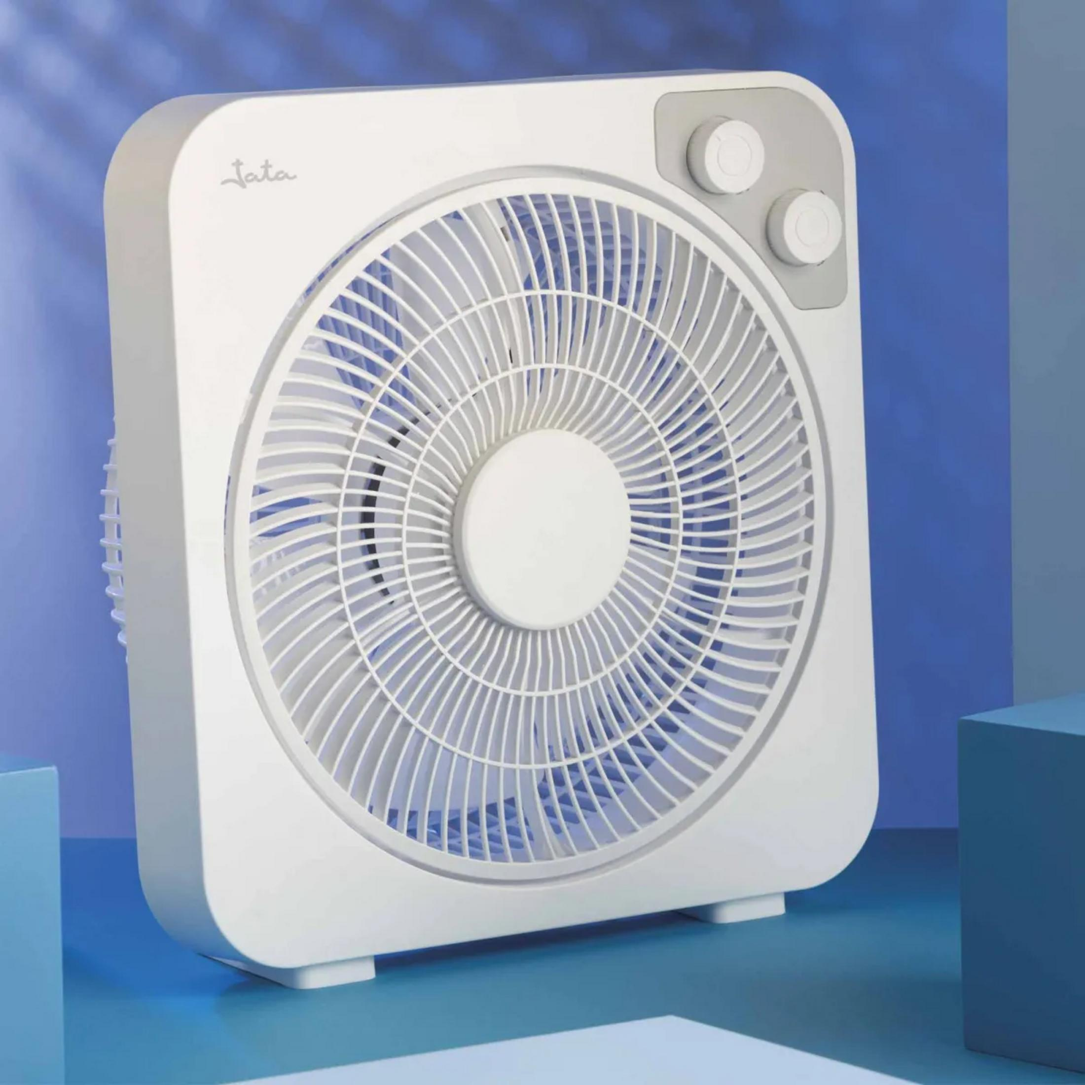 Un ventilador de caja blanco con fondo azul y dos perillas de control arriba.