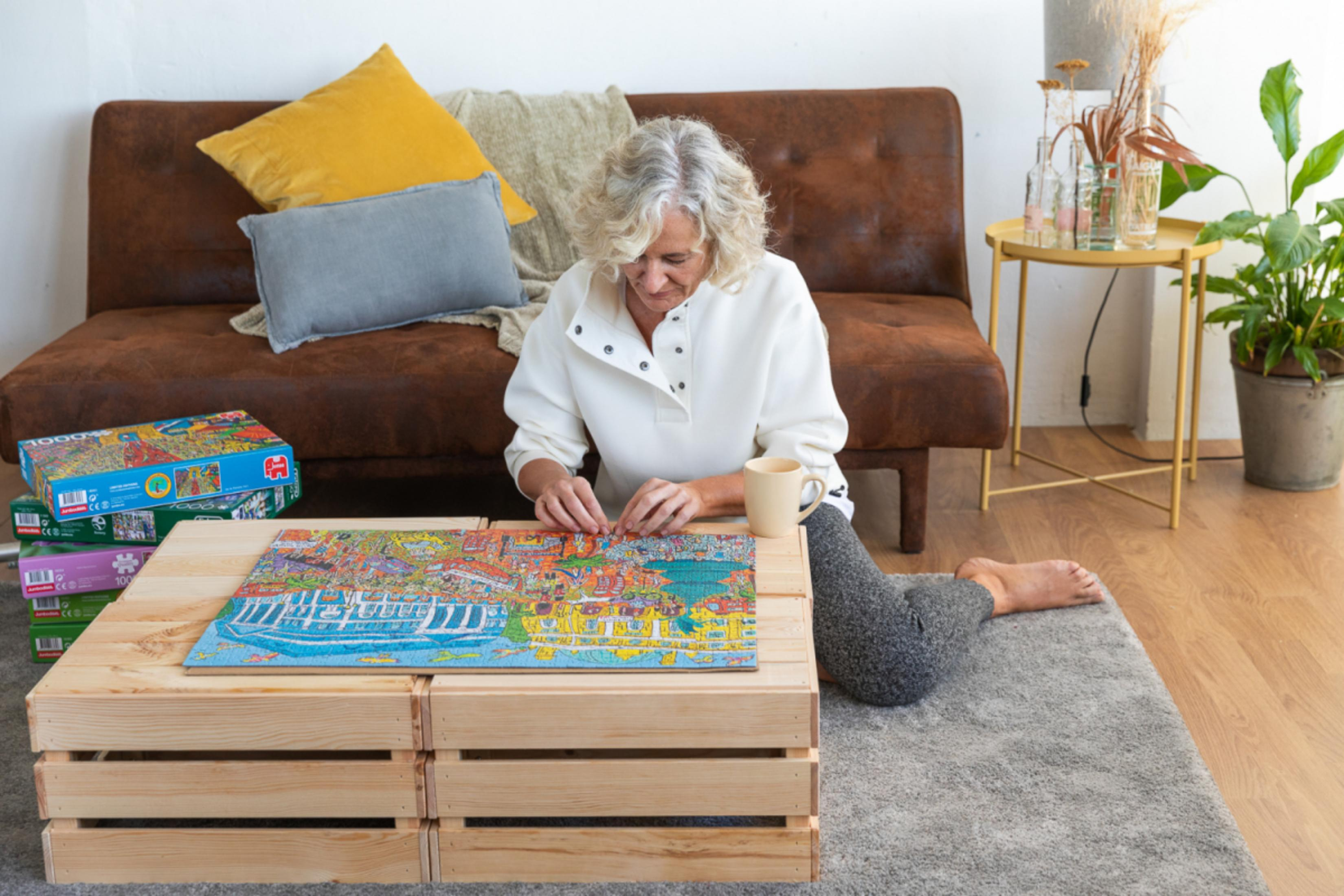 Una donna seduta a terra fa un puzzle. Un divano marrone sullo sfondo.