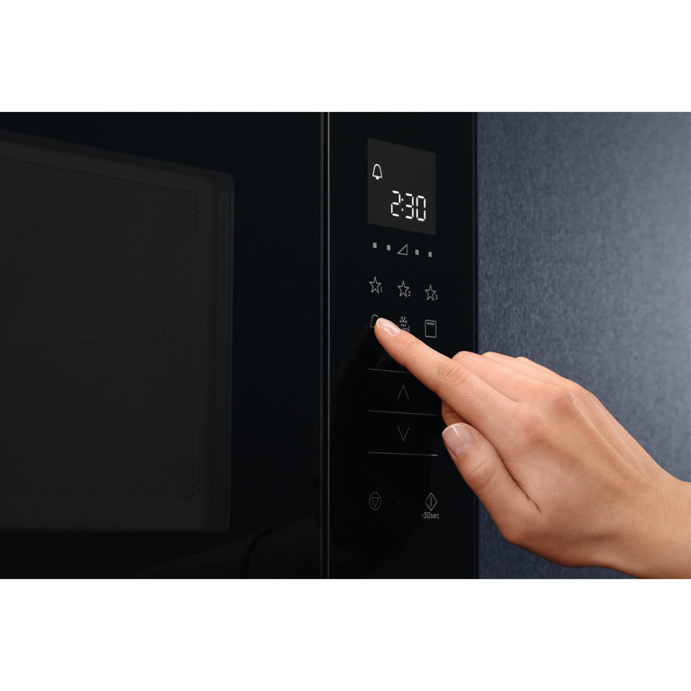 Una mano presiona un botón en el panel de control de un microondas negro.
