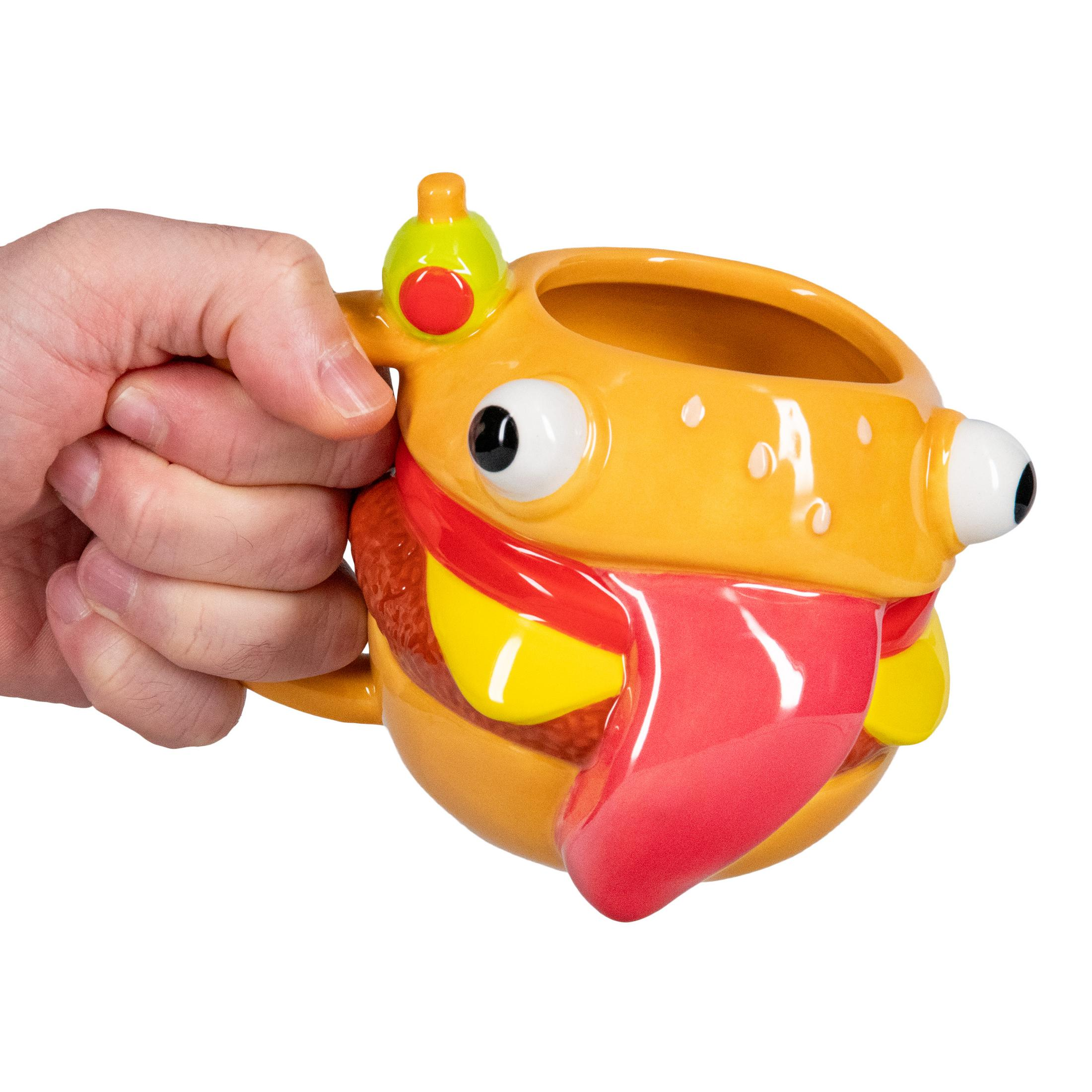 Una mano sostiene una taza de hamburguesa amarilla con ojos y lengua roja.