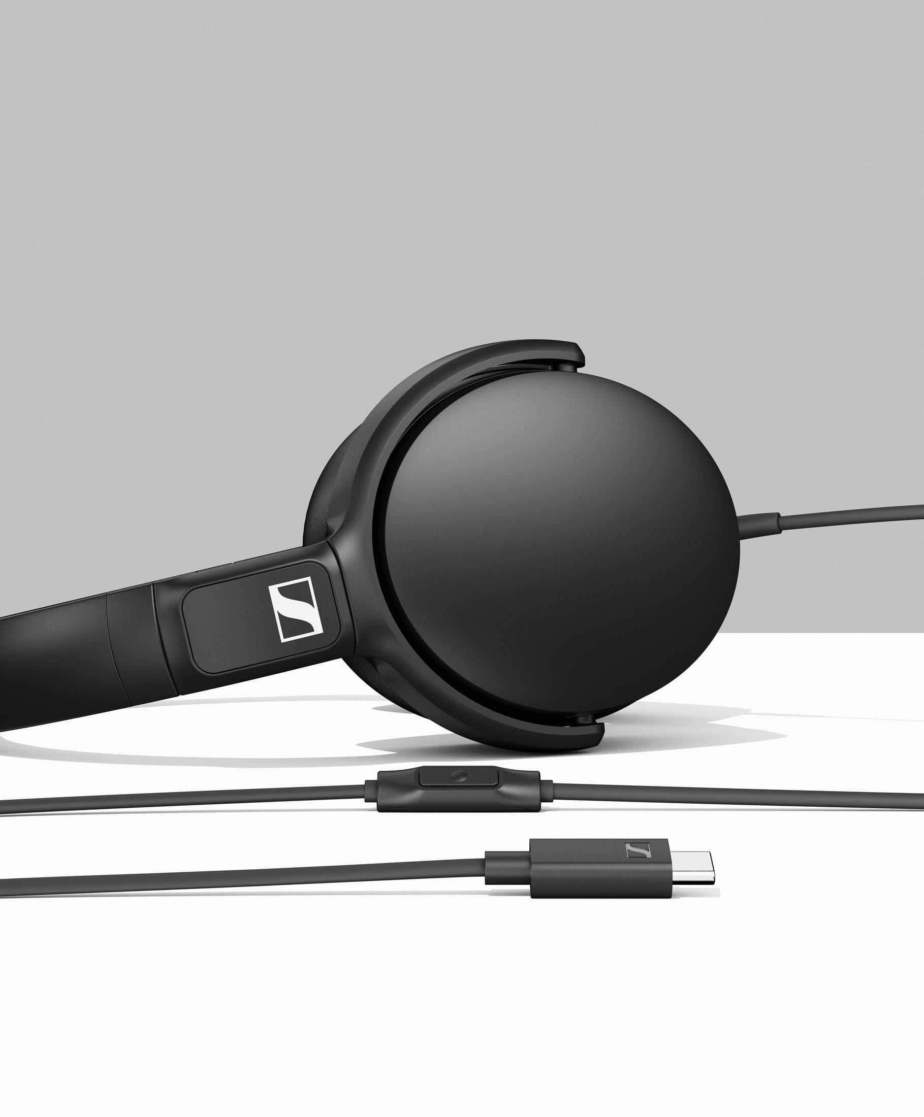 Auriculares negros con cable y conector USB-C sobre fondo gris.
