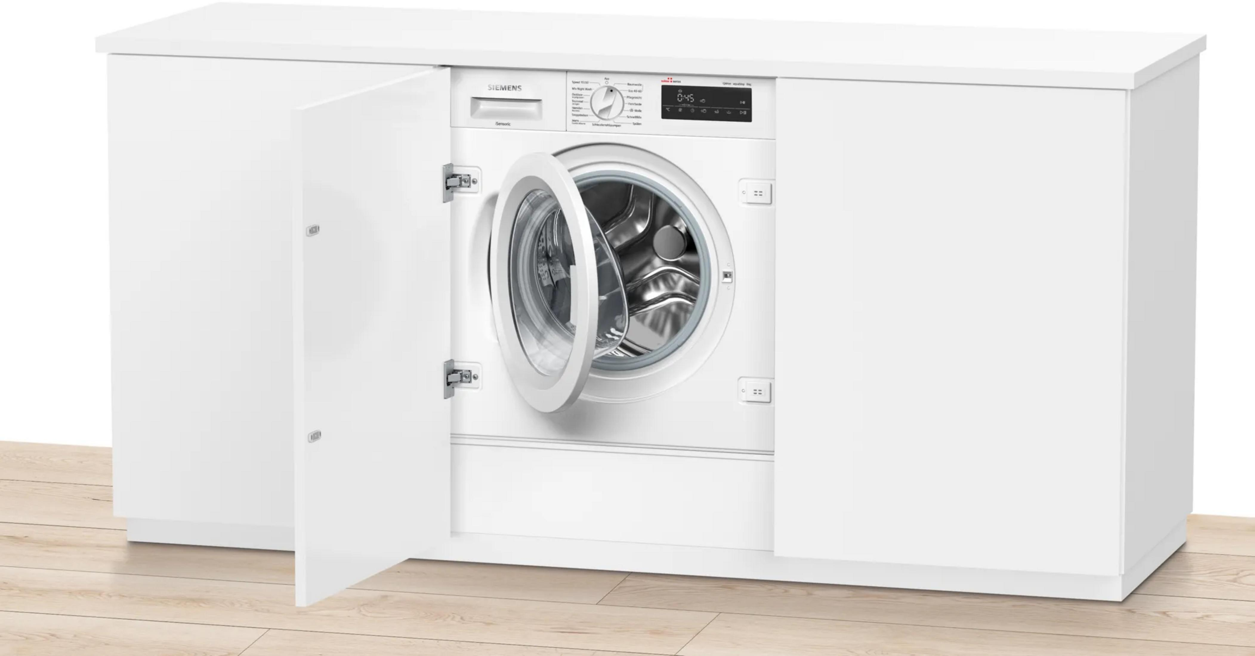 Eine weiße Waschmaschine mit geöffneter Tür in einem weißen Schrank, auf Holzboden.