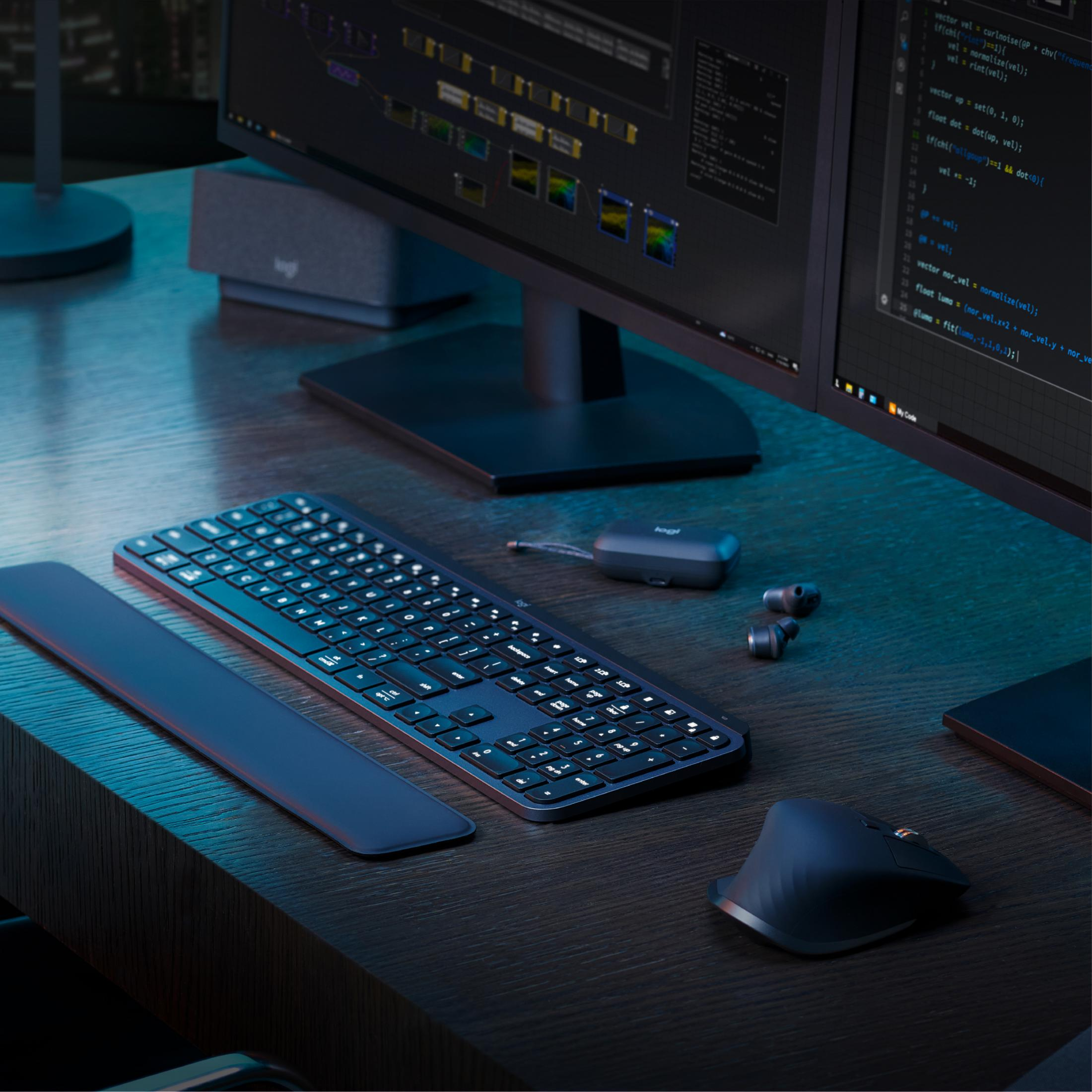 Un escritorio oscuro con teclado, ratón, auriculares y monitores mostrando código.
