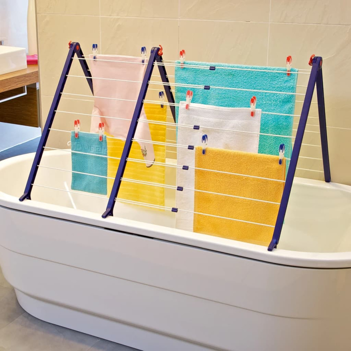 Ein zusammenklappbarer Wäscheständer mit bunten Handtüchern trocknet über einer Badewanne.