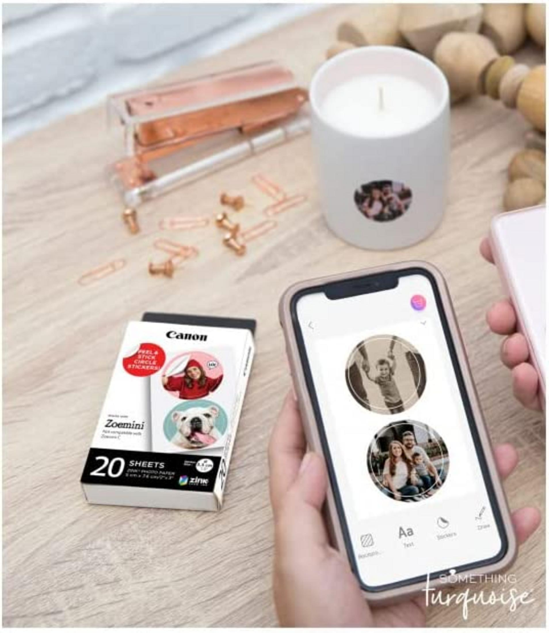 Un paquete Canon Zoemini con pegatinas, una vela y un teléfono mostrando fotos.