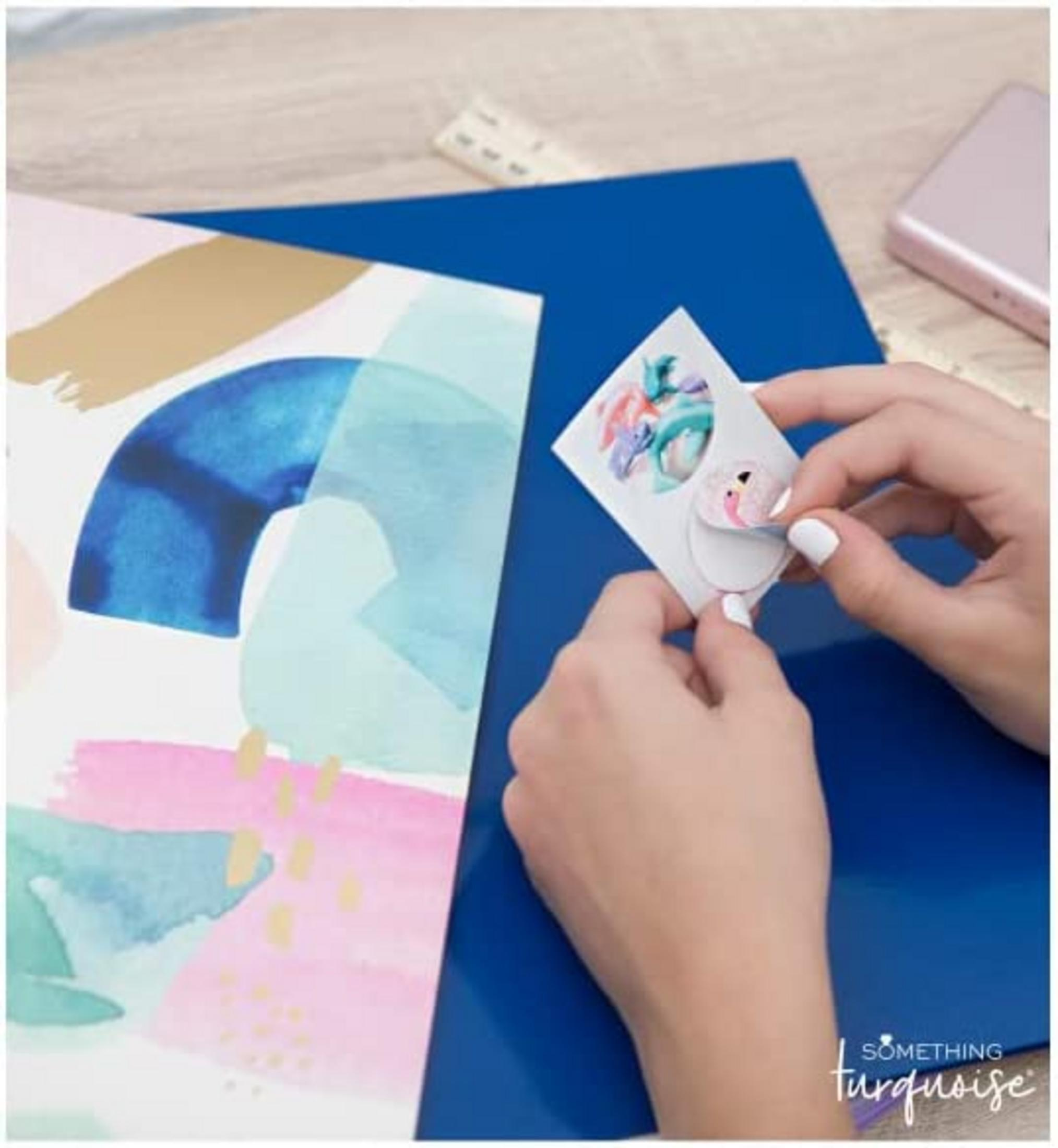 Manos despegando un adhesivo de flamenco de su soporte, junto a un cuaderno.