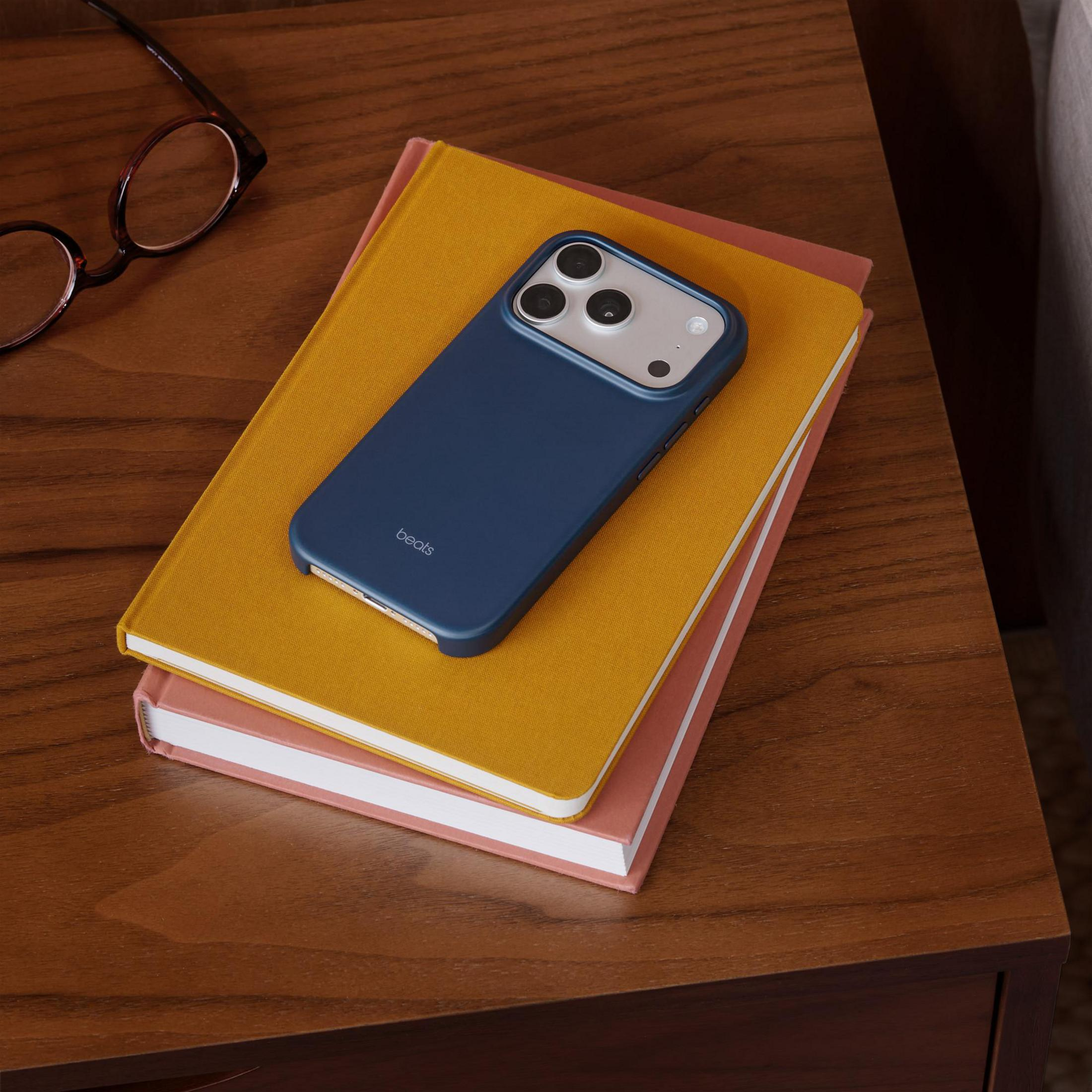 A blue phone in a case rests on two books on a wooden table.