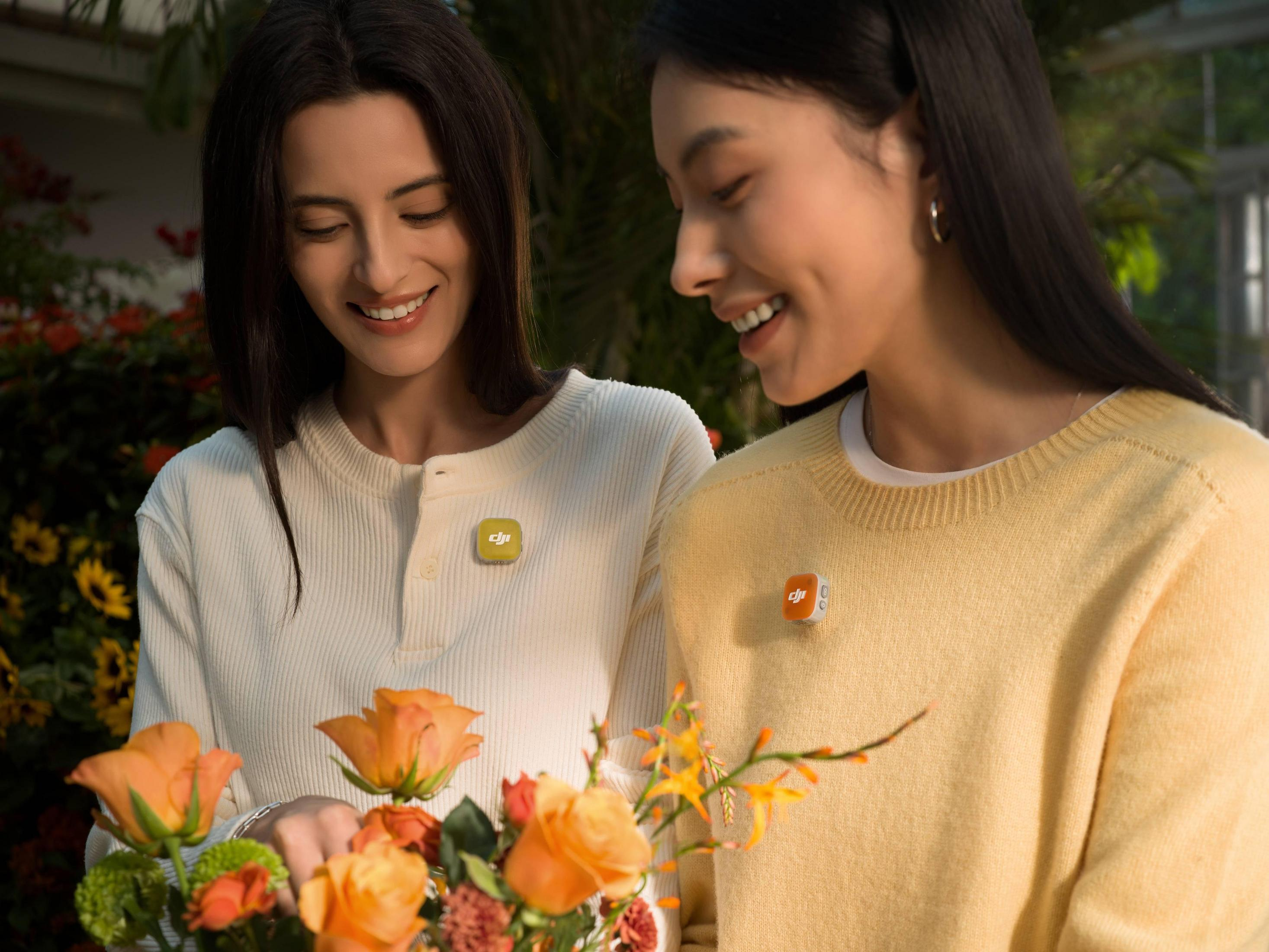 Dos mujeres sonrientes con flores y pines DJI en sus suéteres.