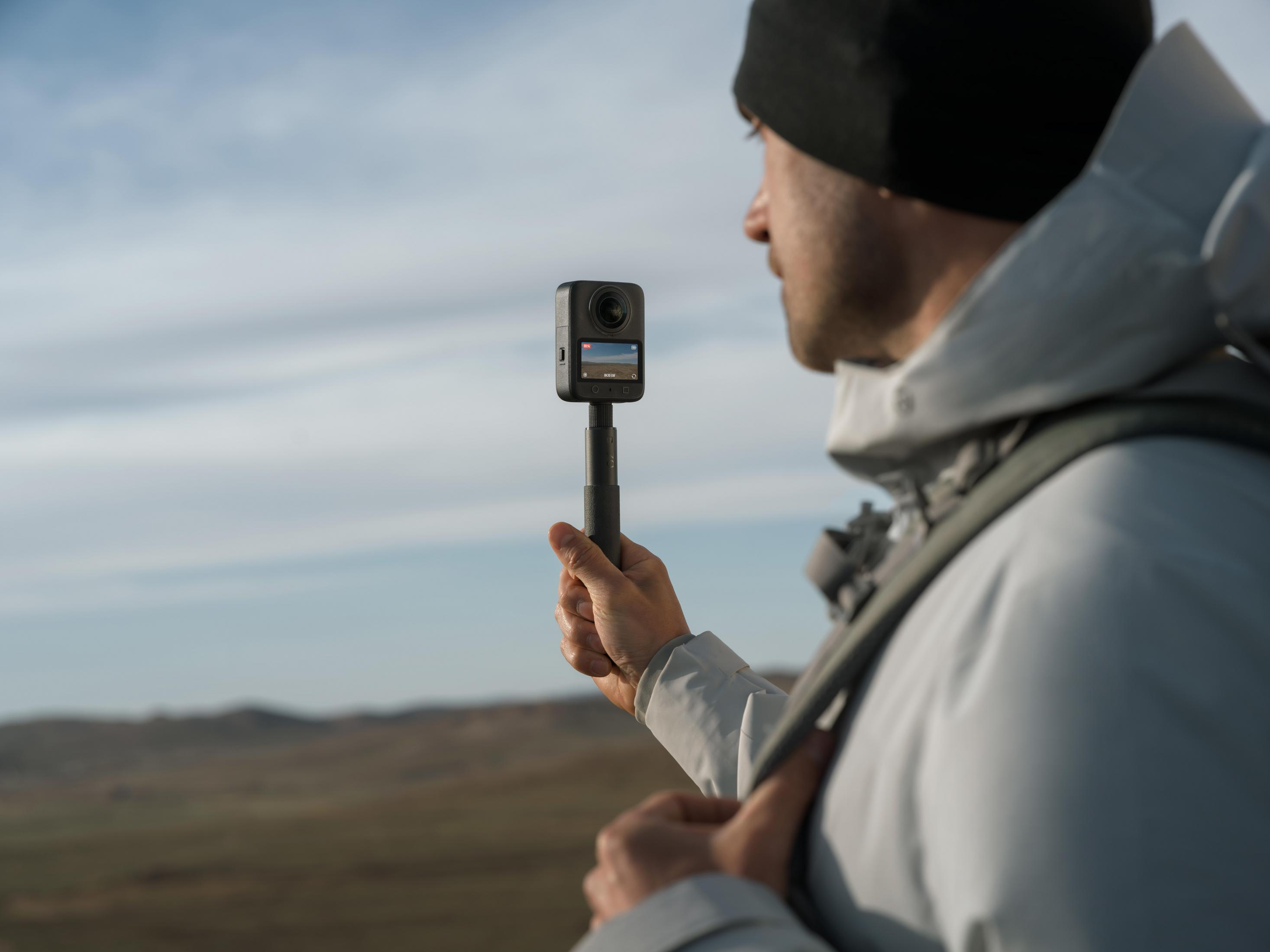Mann mit schwarzer Mütze hält 360-Kamera in felsiger Landschaft.
