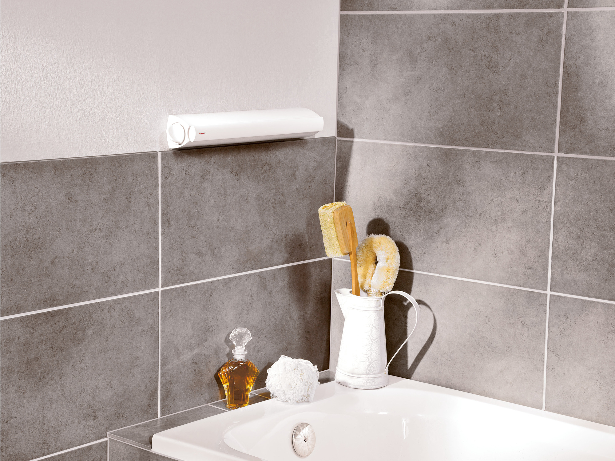 Eine weiße Badewanne mit Badeaccessoires: ein weißer Krug mit Bürsten, einer Parfümflasche und einem Badeschwamm.