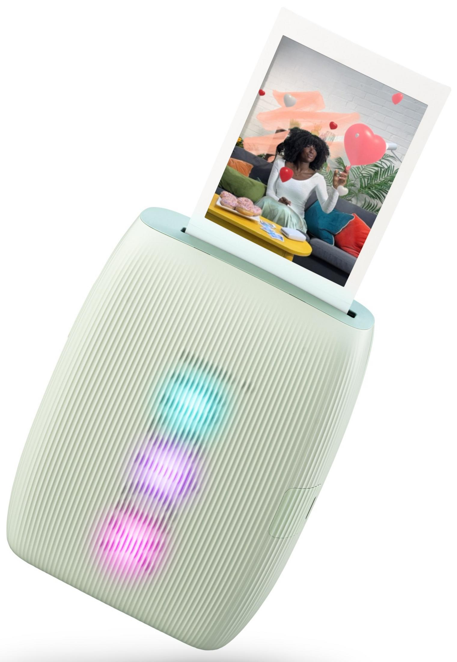 Una stampante verde menta emette una foto polaroid di una donna seduta con palloncini a forma di cuore.