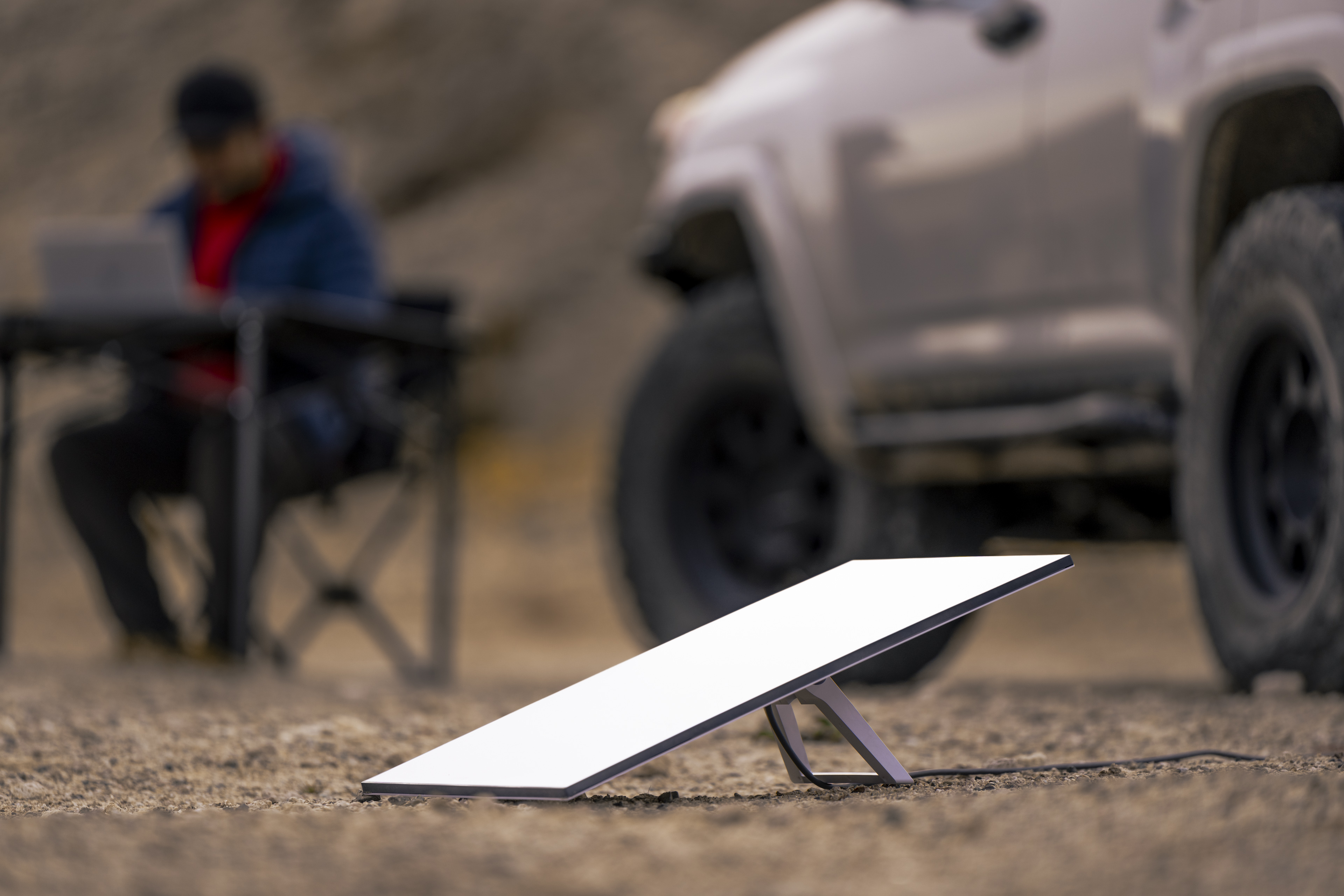Un panel de internet satelital blanco en el suelo, hombre en laptop, SUV detrás.