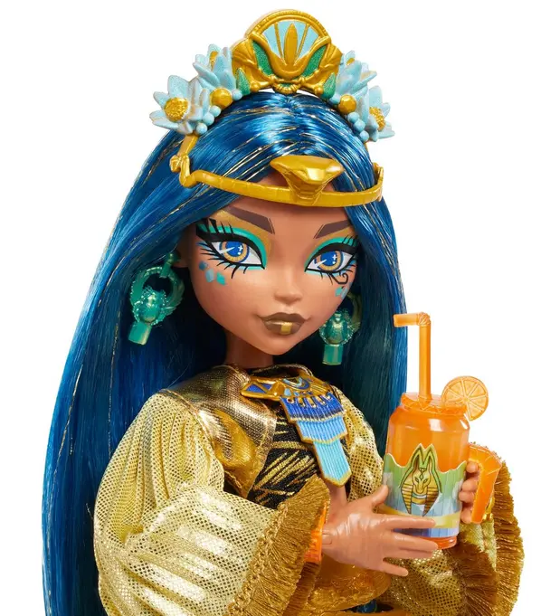 Puppe mit blauen Haaren, goldener Krone, goldenem Kleid, hält ein oranges Getränk mit Strohhalm.