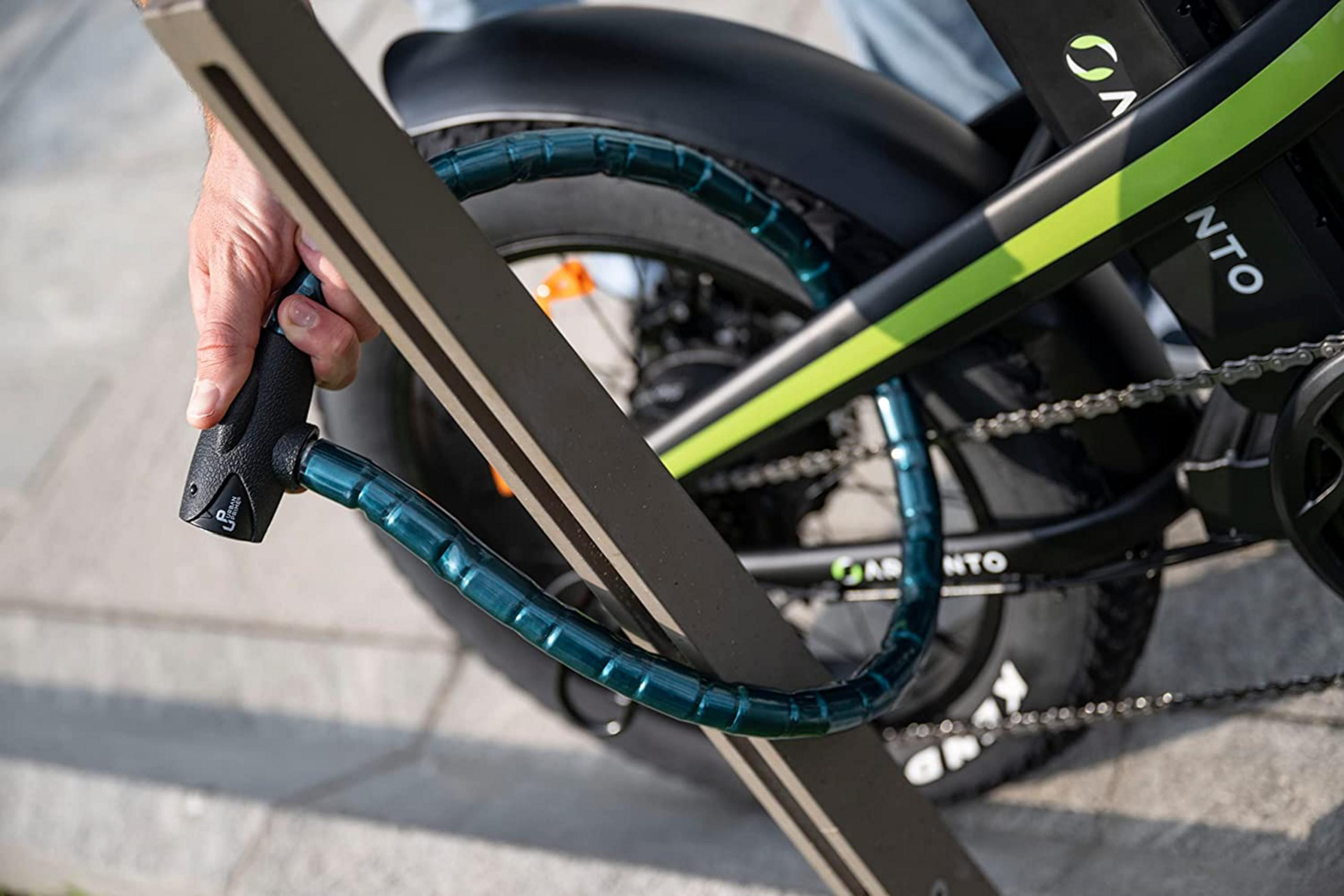 Un hombre asegura con candado la rueda trasera de una bici negra con detalles verdes.